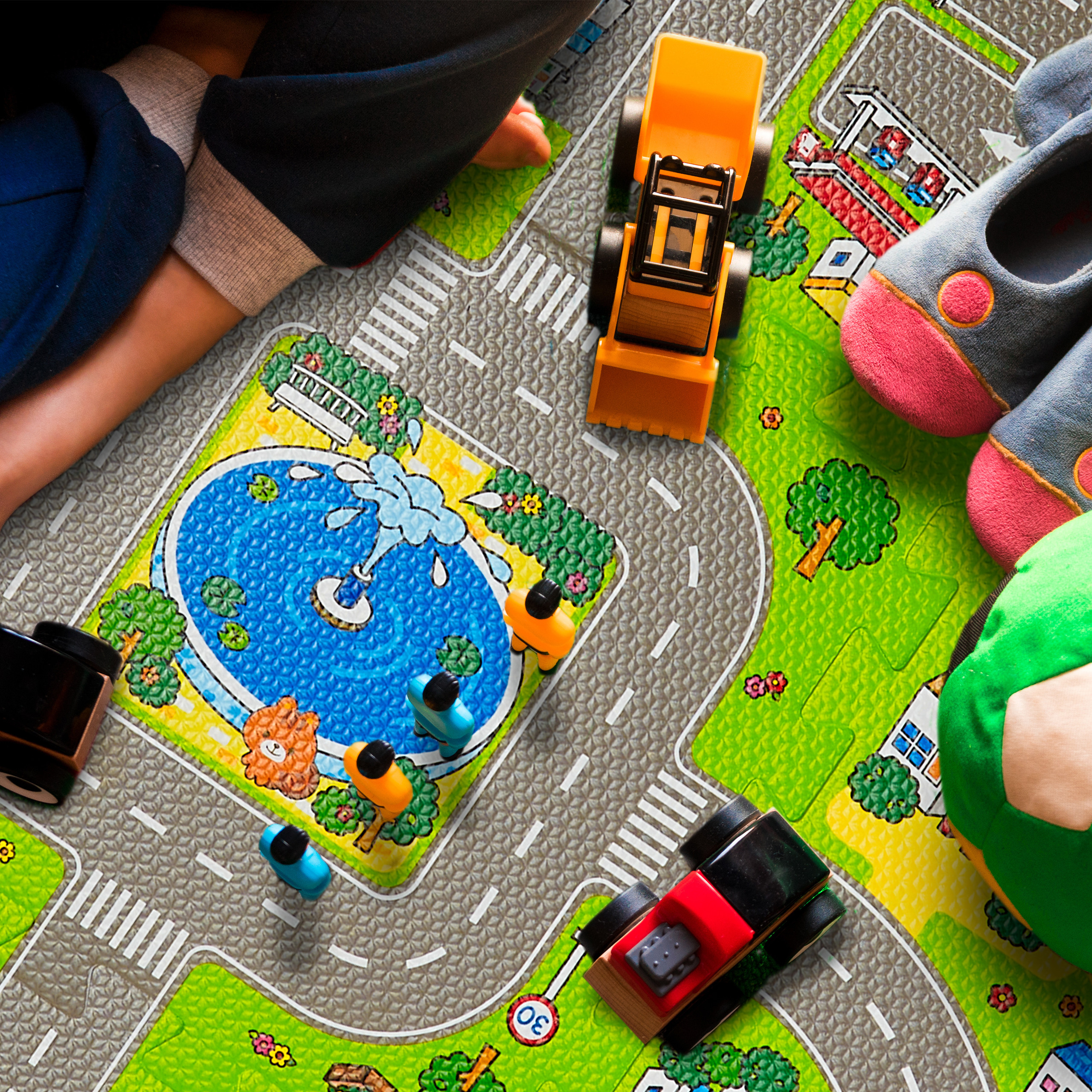 Ein Kind sitzt auf einer Spielmatte mit Straßen, einer großen Springbrunnenillustration und bunten Spielzeugautos.