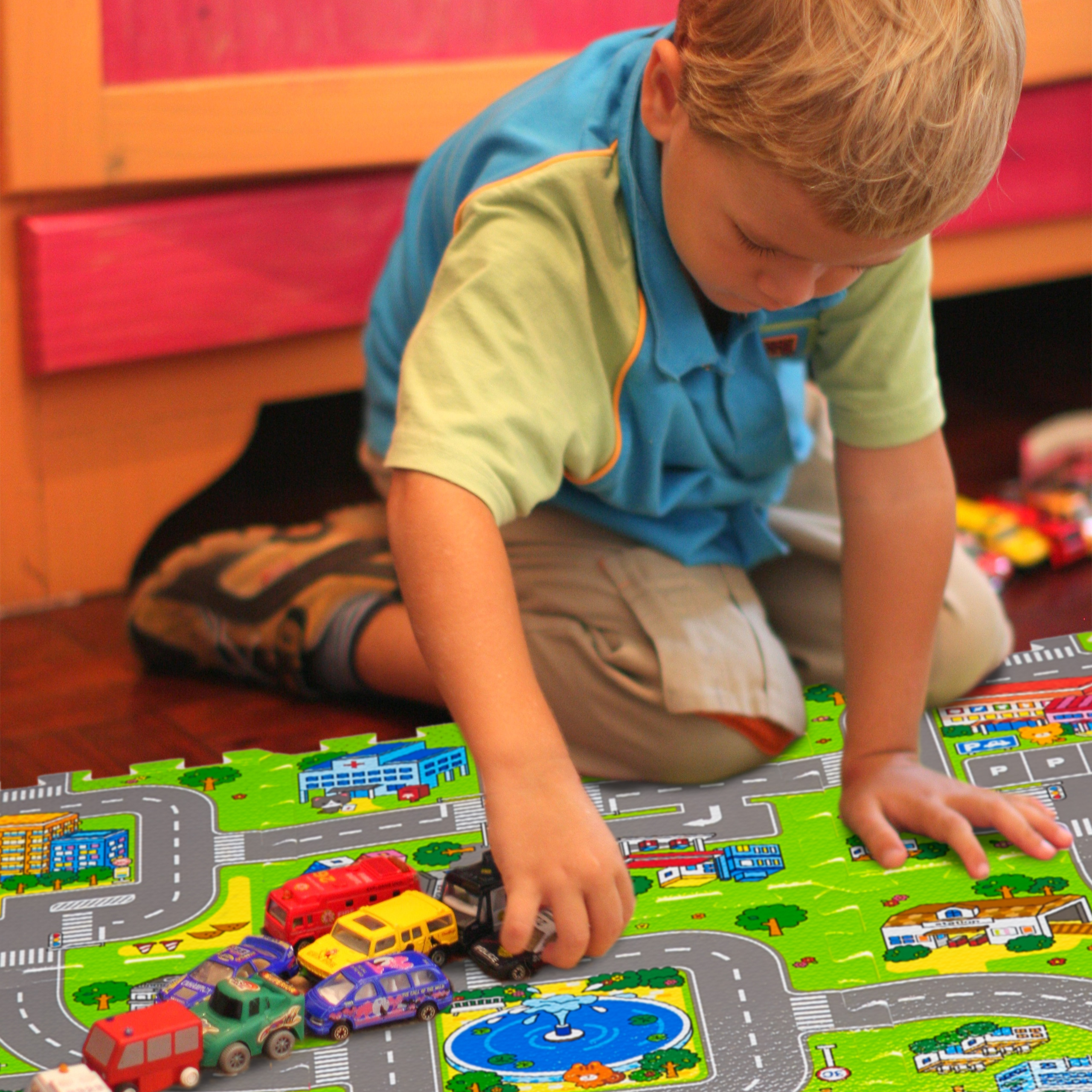Ein junger Junge sitzt auf dem Boden und spielt mit Spielzeugautos auf einer bunten Straßenkarte.