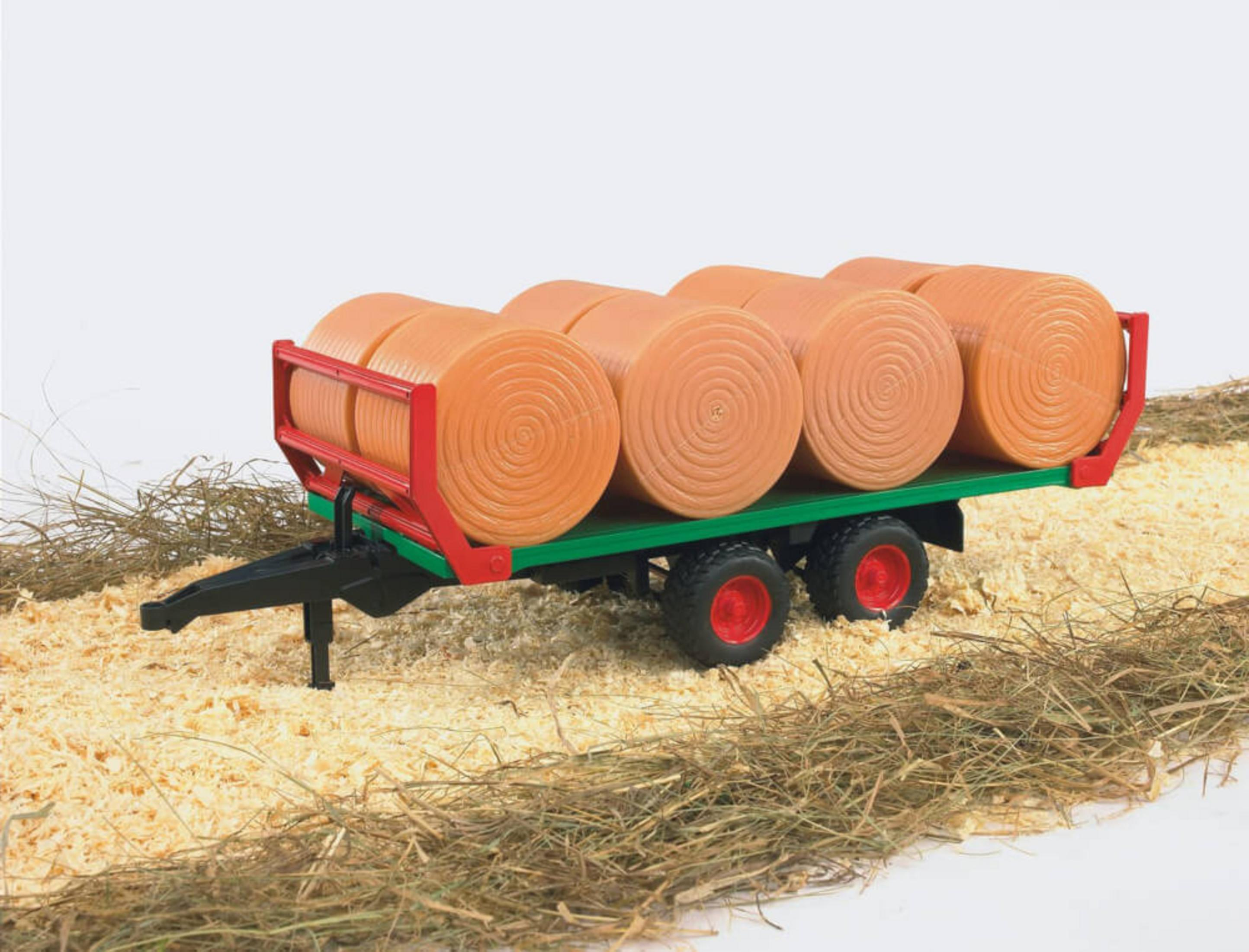Ein grüner und roter Spielzeug-Landwirtschaftsanhänger mit acht orangen Rundballen auf Stroh.