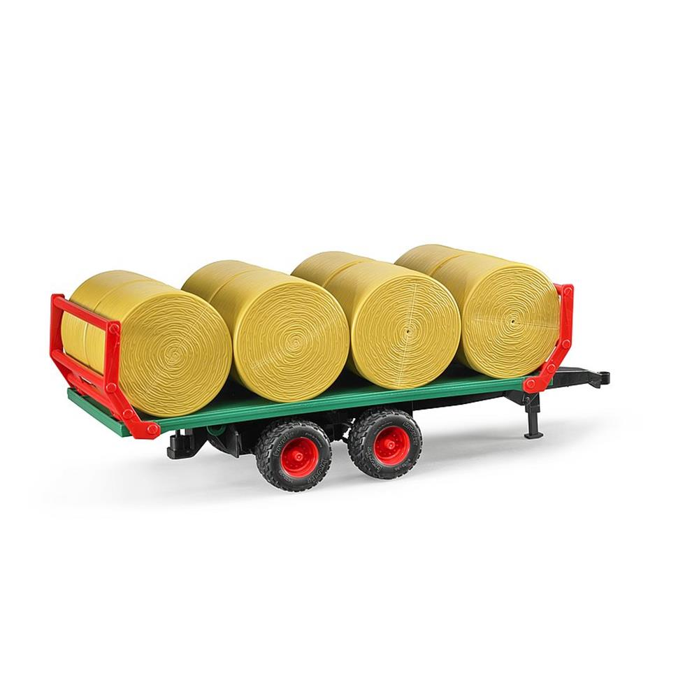 Ein grüner Spielzeugtraktoranhänger mit roten Rädern transportiert vier große gelbe Heuballen auf weißem Grund.