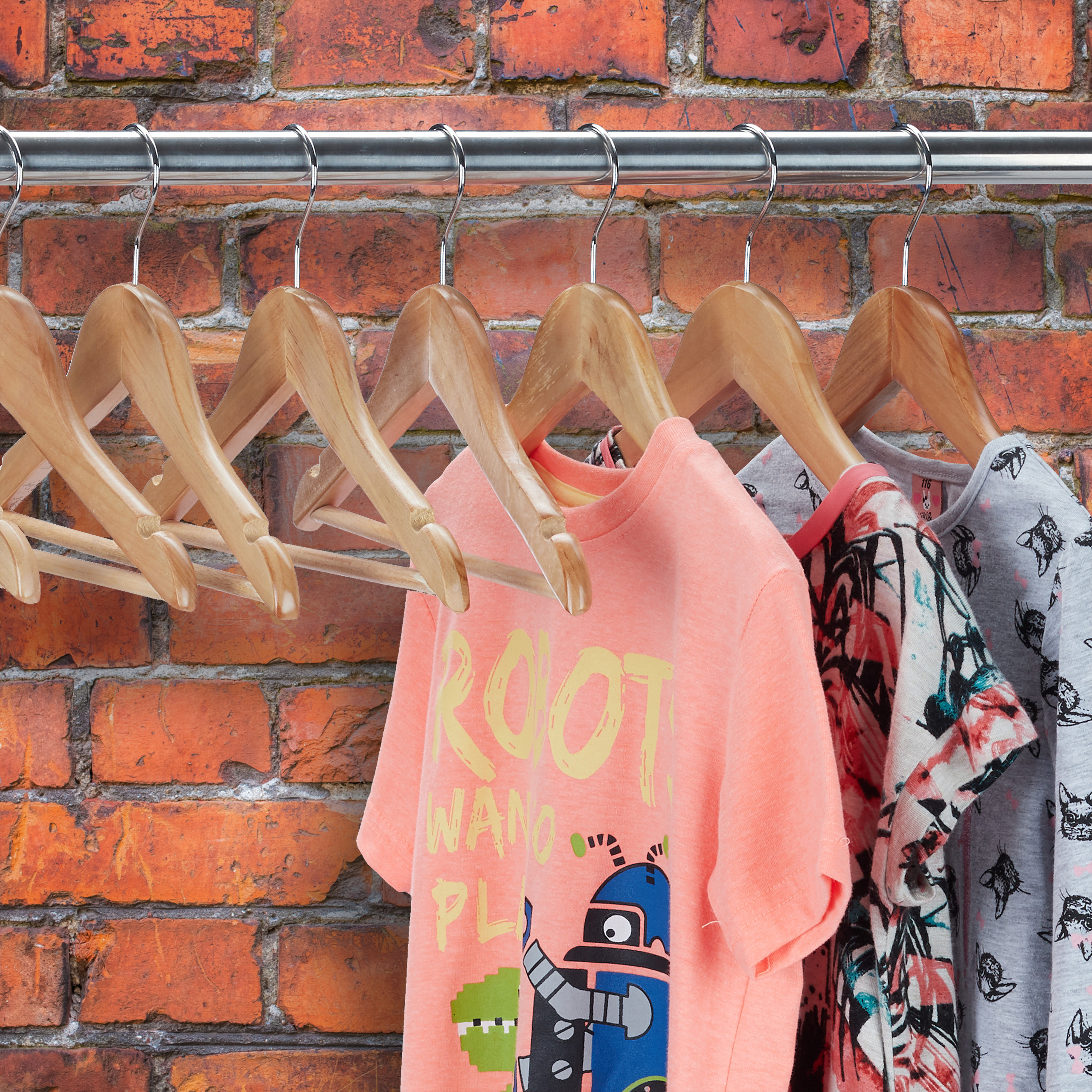 Kleiderbügel hängen an einer Stange vor einer roten Backsteinwand, einige tragen bunte T-Shirts.