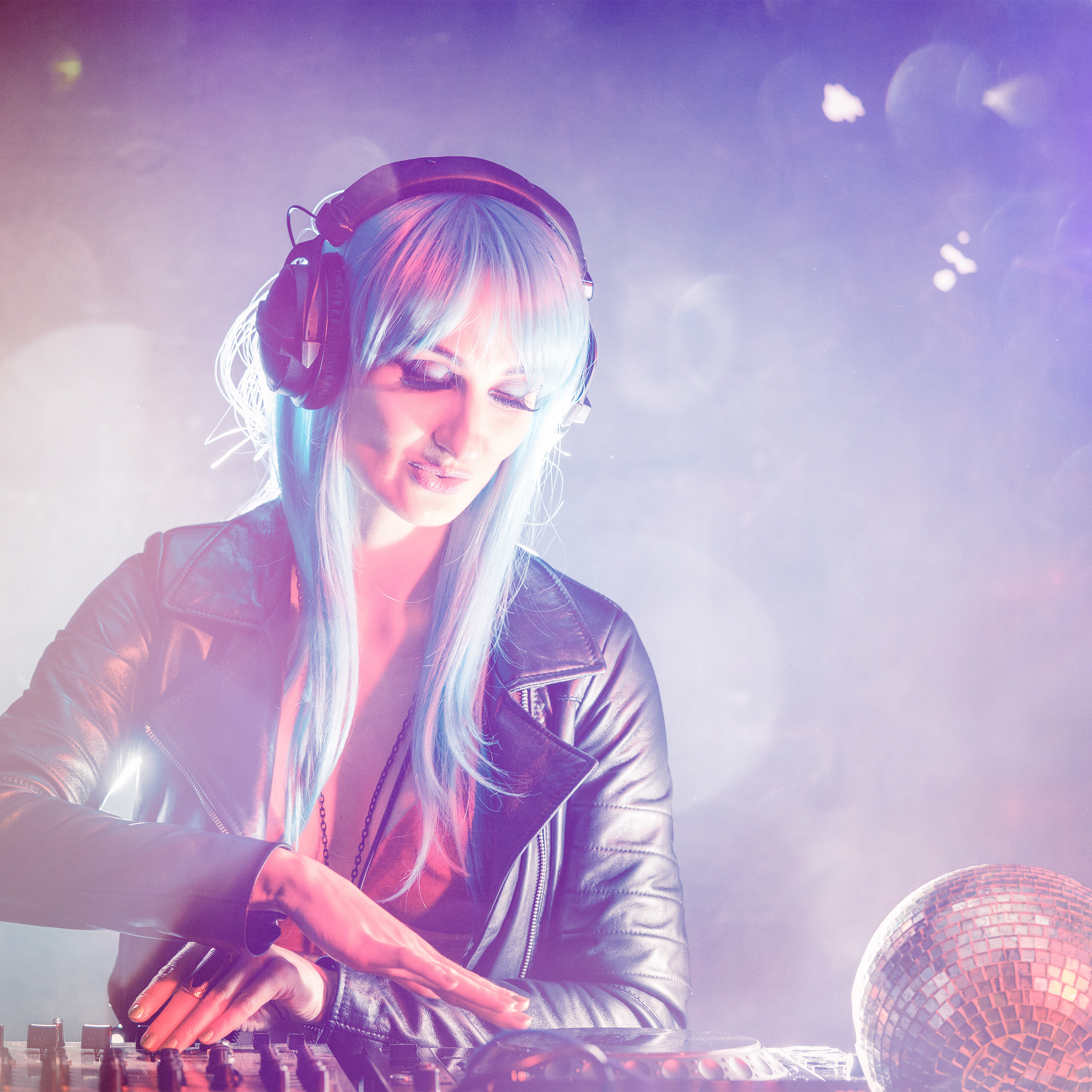 DJ mit blauen Haaren und Kopfhörern mixt Musik am Mischpult im Club.
