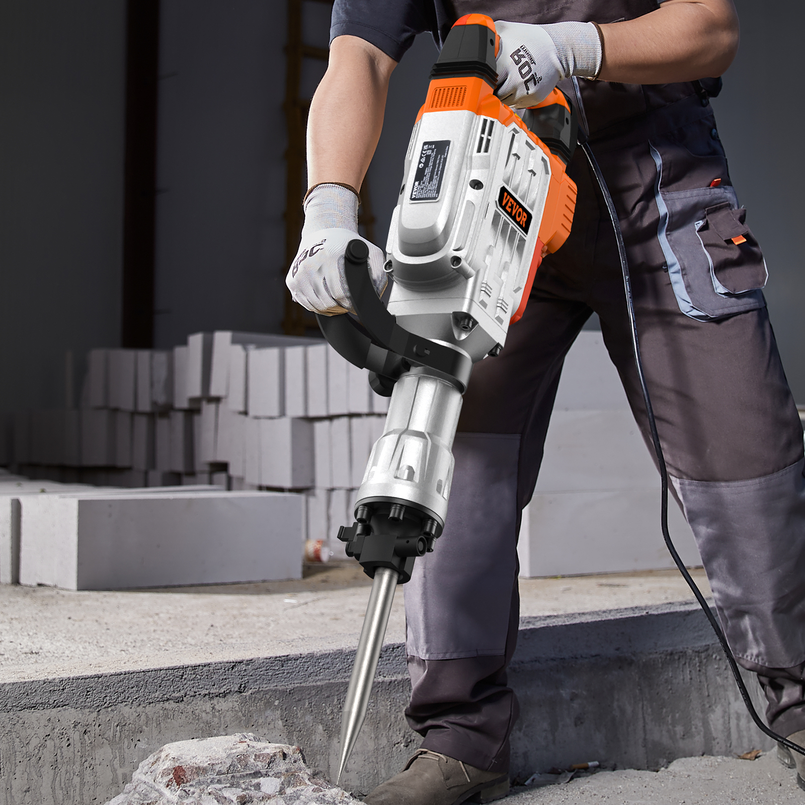Un trabajador con ropa de trabajo gris y guantes sostiene un martillo demoledor naranja y plateado.