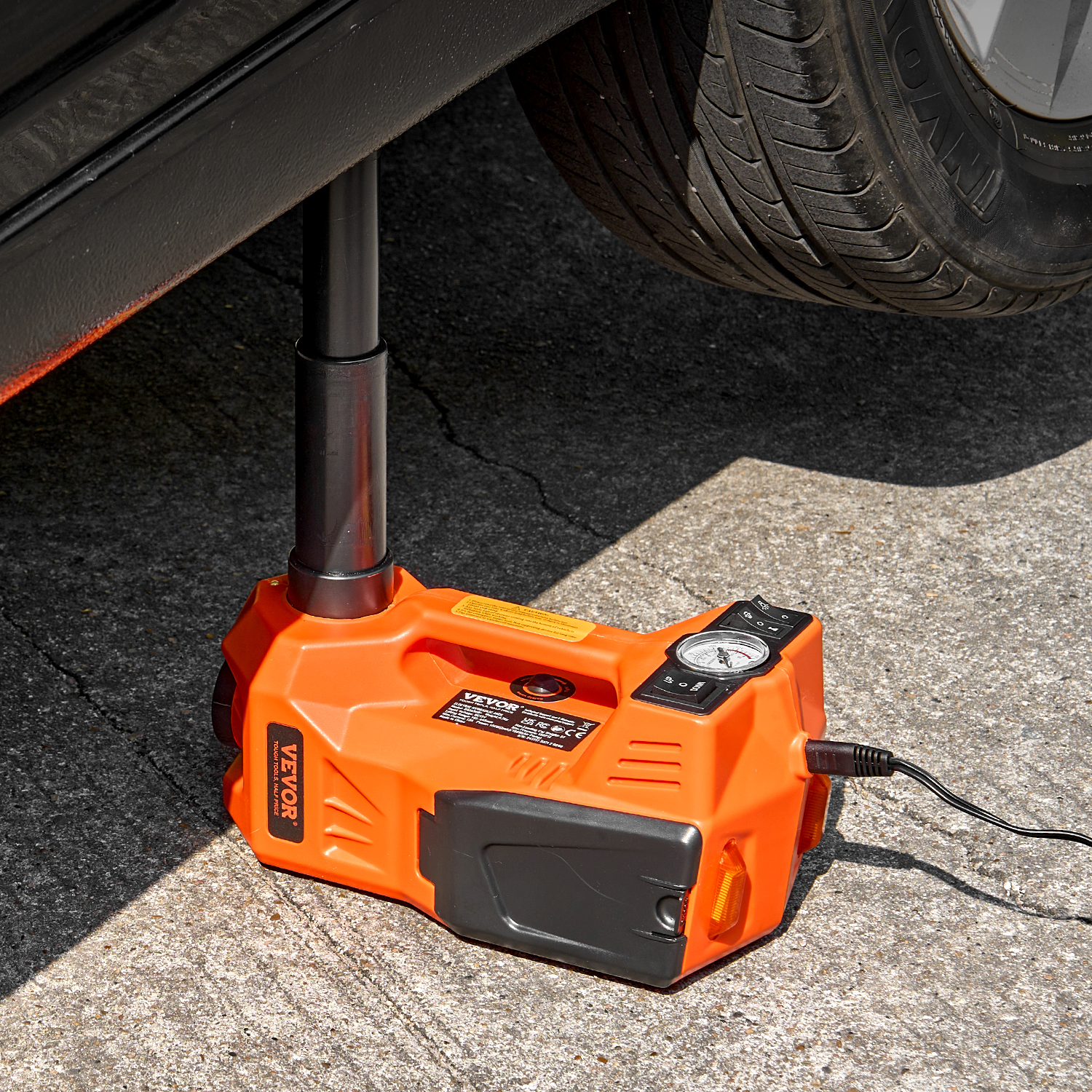 Un gato de coche eléctrico naranja levantando un coche en pavimento de asfalto.