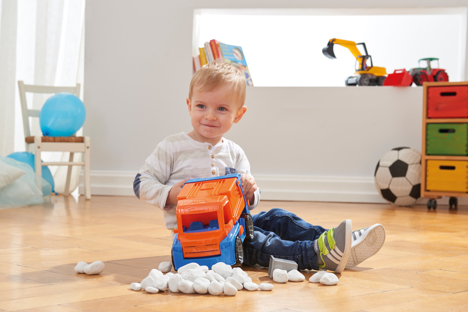 Niño pequeño sentado en el suelo de madera, jugando con un gran camión de juguete.