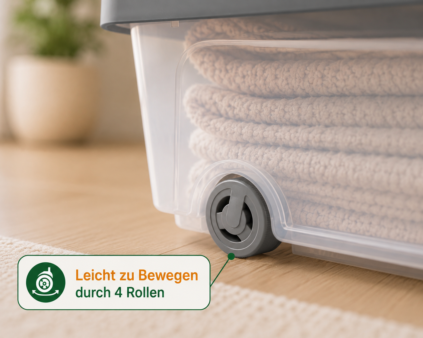 Transparente Aufbewahrungsbox mit grauen Rollen und gefalteten Decken im Inneren auf einem Holzfussboden.