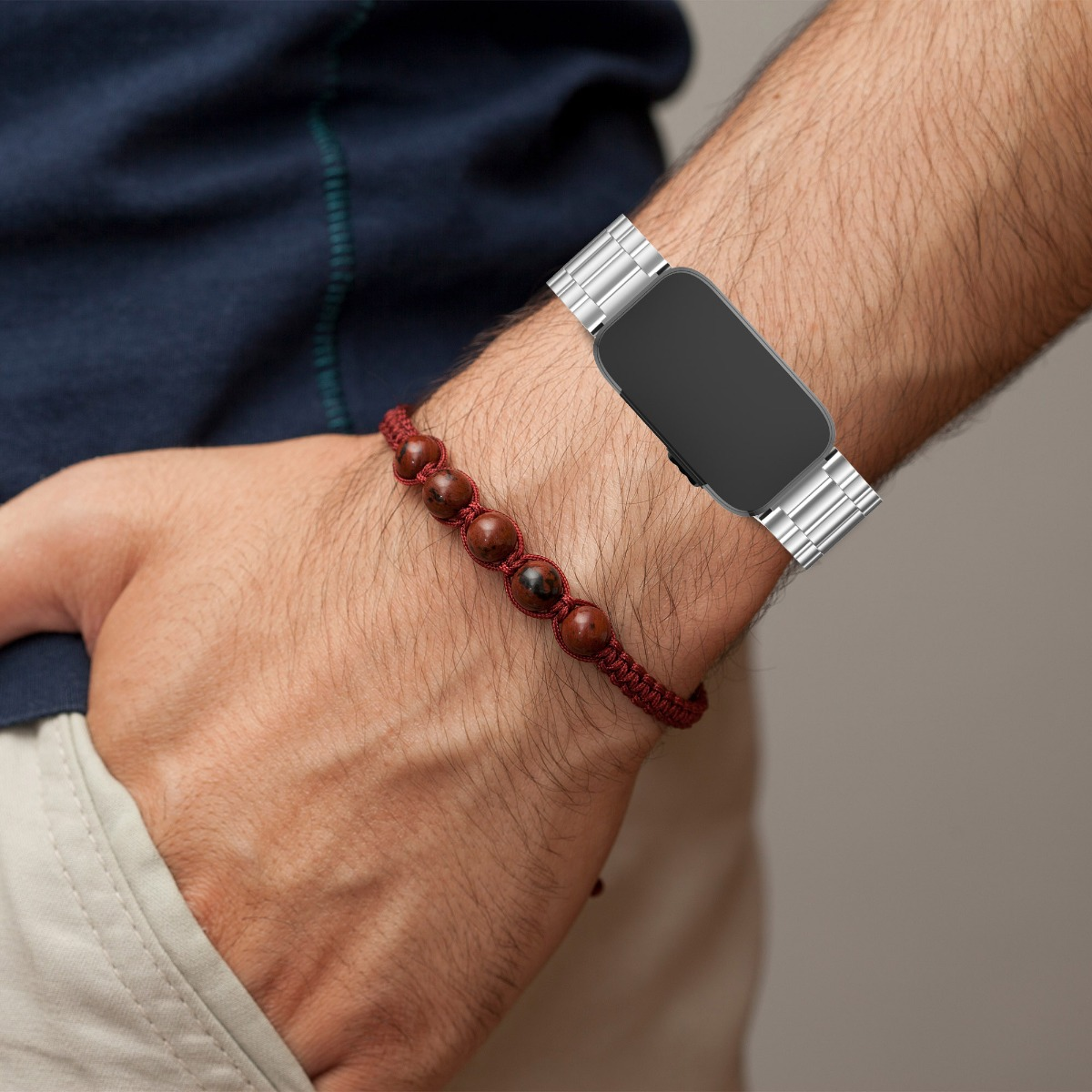 Ein Handgelenk mit einer Smartwatch mit Metallarmband und einem braunen Perlenarmband.