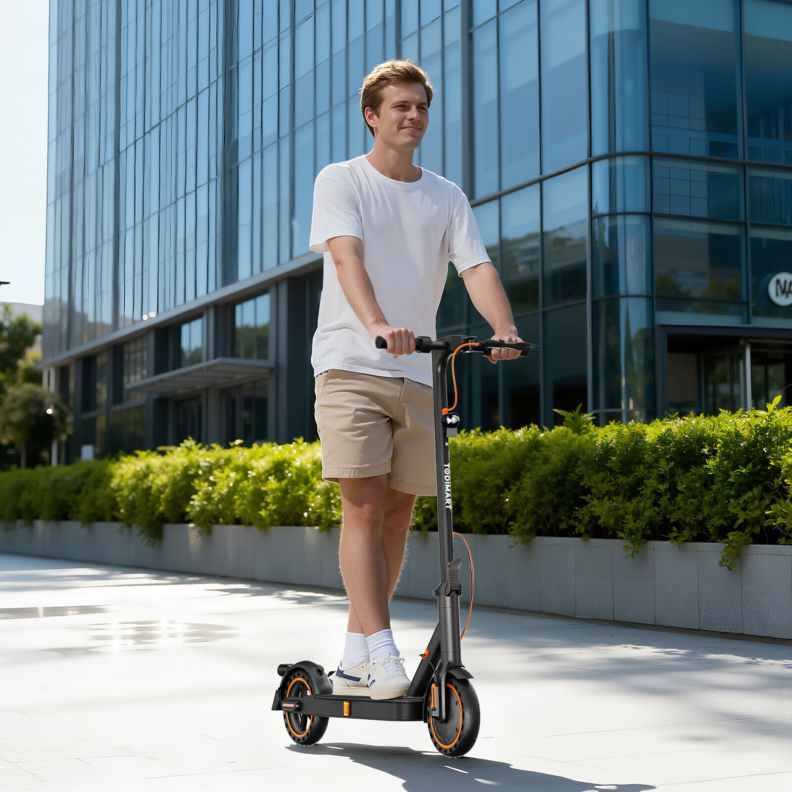 Ein junger Mann fährt auf einem schwarzen E-Scooter vor einem modernen Gebäude mit Glasfassade.