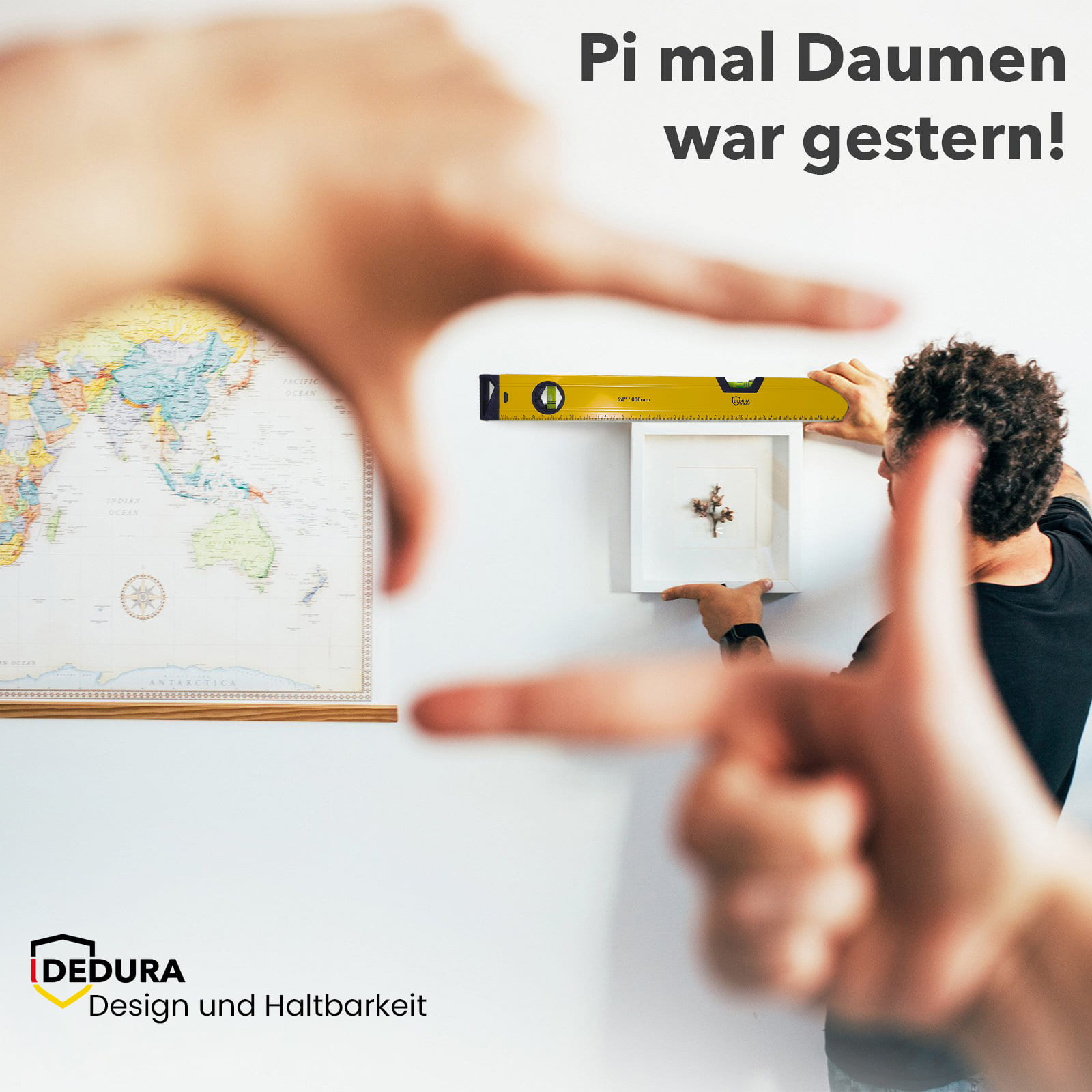 Ein Mann richtet ein gerahmtes Bild mit einer Wasserwaage aus, während Hände im Vordergrund es einrahmen.