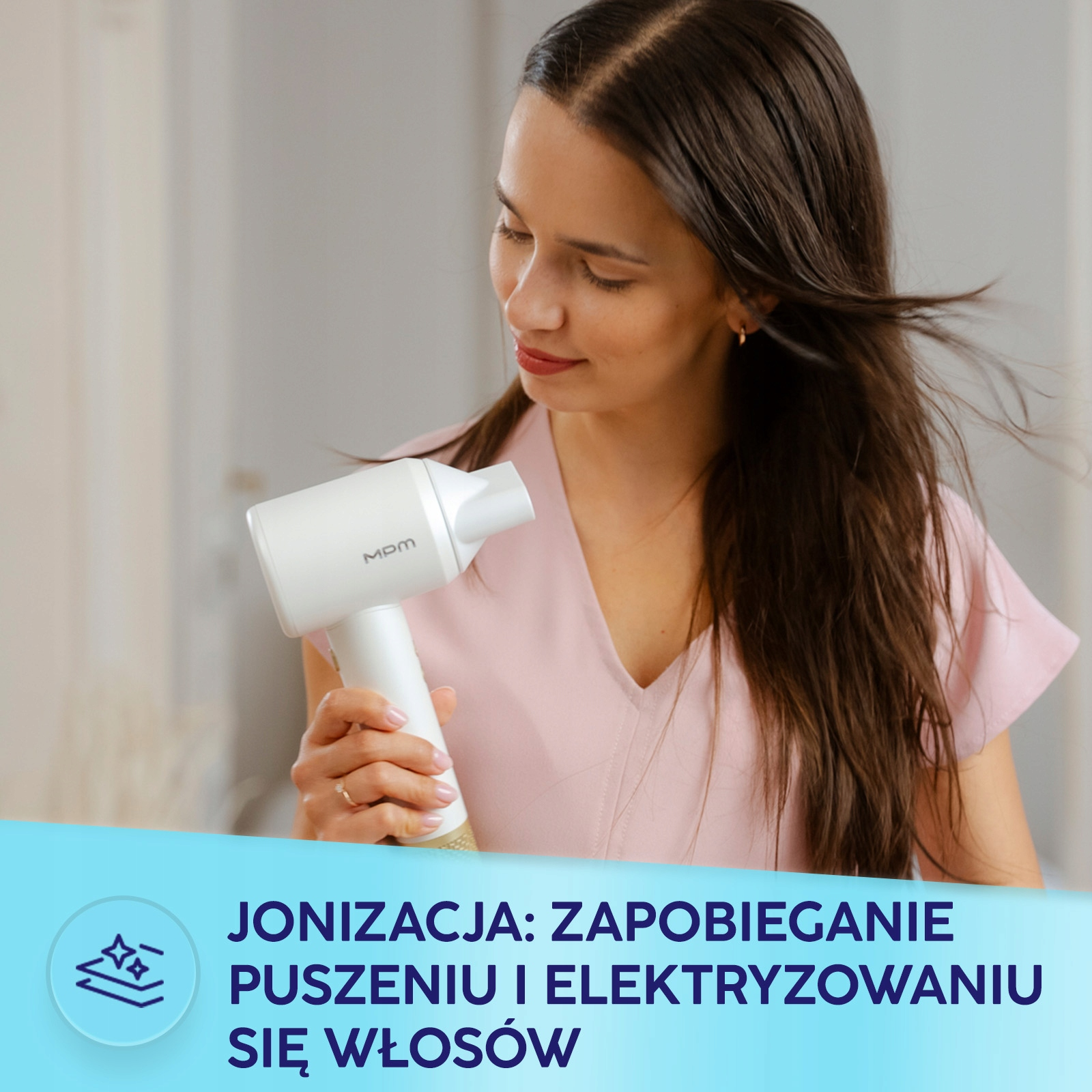 Kobieta w różowej bluzce trzyma w ręku białą suszarkę do włosów.
