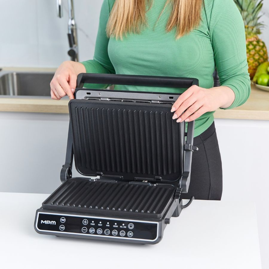 Kobieta w zielonej koszuli otwiera elektryczny grill stołowy w kuchni.