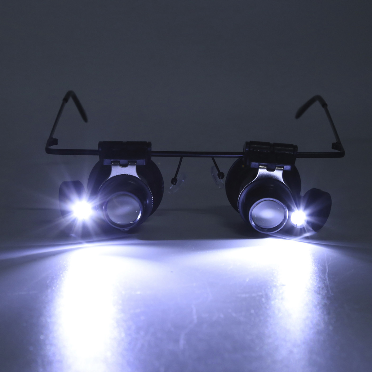 Schwarze Lupenbrille mit zwei integrierten LEDs, die helles Licht auf eine Oberfläche werfen.
