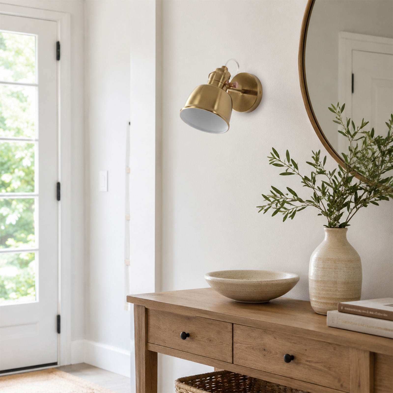 Lámpara de pared dorada sobre mesa de madera con jarrón, cuenco y libros contra una pared blanca.