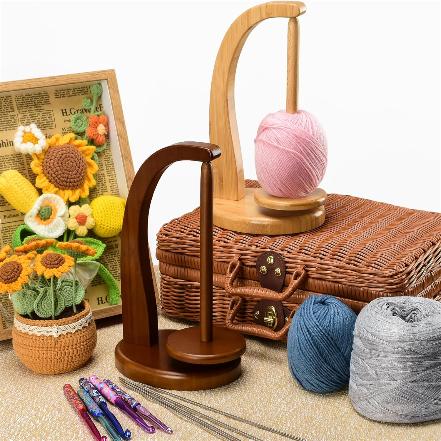 Zwei Garnhalter aus Holz, Häkelnadeln, Wollknäuel, ein Weidenkoffer und ein gerahmtes Häkelblumenarrangement.