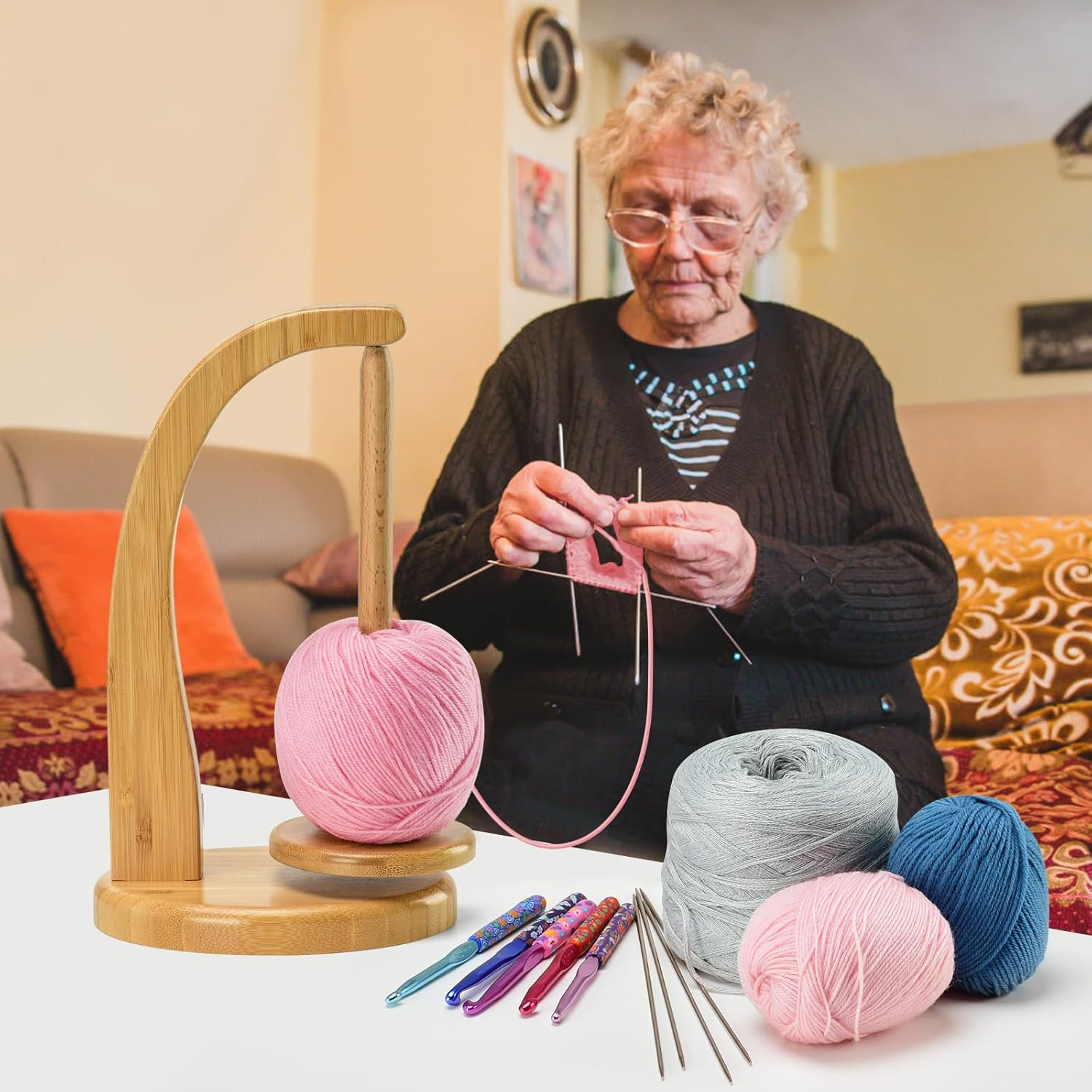 Ältere Frau strickt pinkes Garn; auf dem Tisch liegen mehrfarbige Häkelnadeln und Wollknäuel.