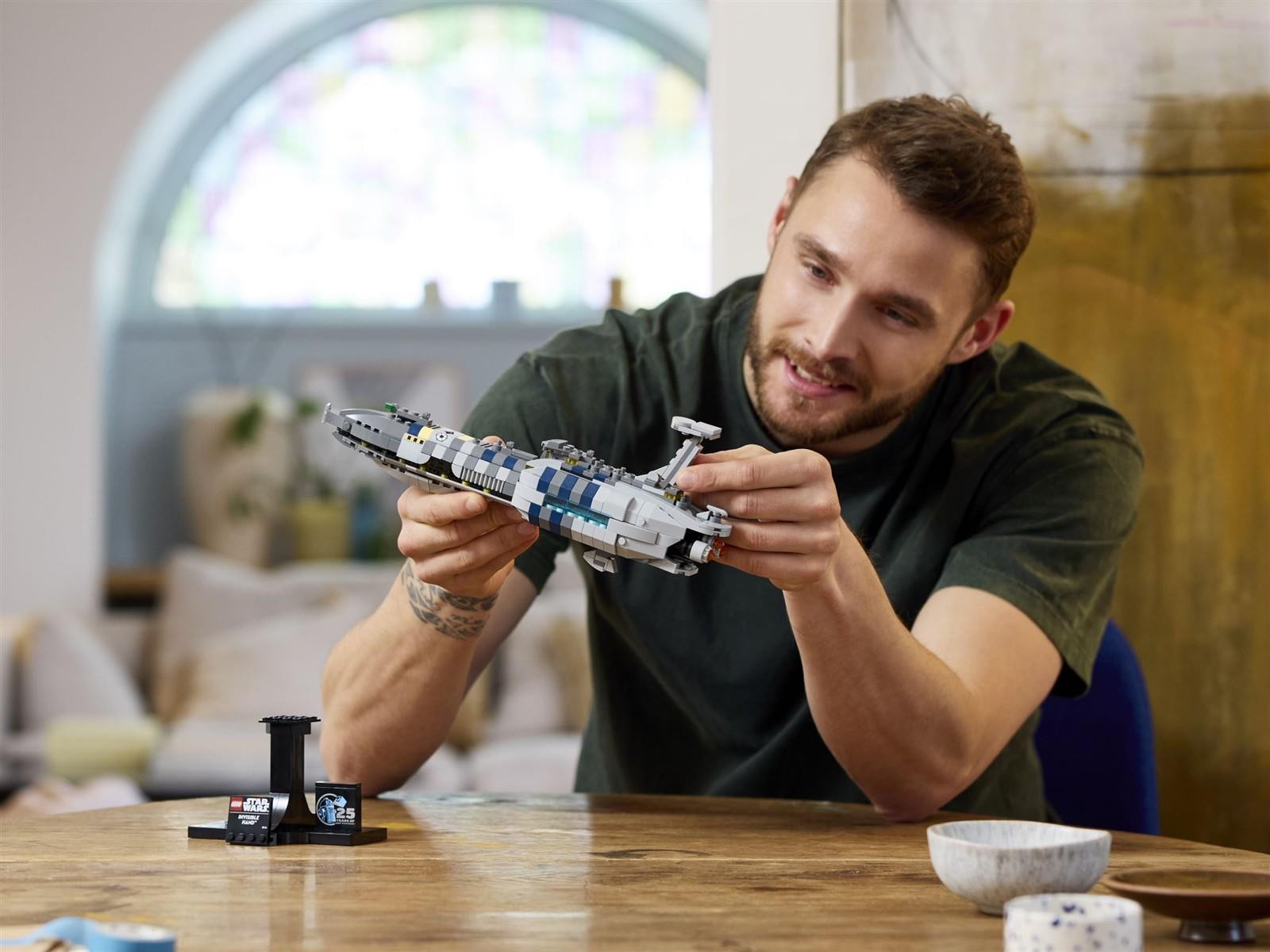 Ein Mann sitzt an einem Holztisch und hält ein graues Lego Star Wars Raumschiff in den Händen.