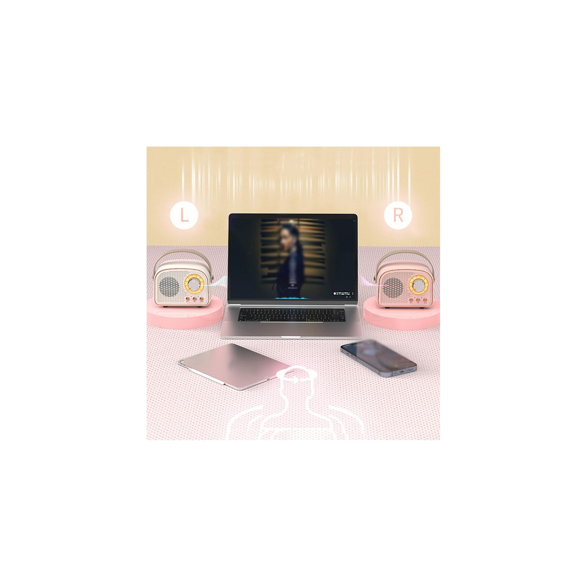 Ein Laptop steht auf einem Tisch zwischen zwei kleinen rosafarbenen Lautsprechern, einem Tablet und einem Smartphone.