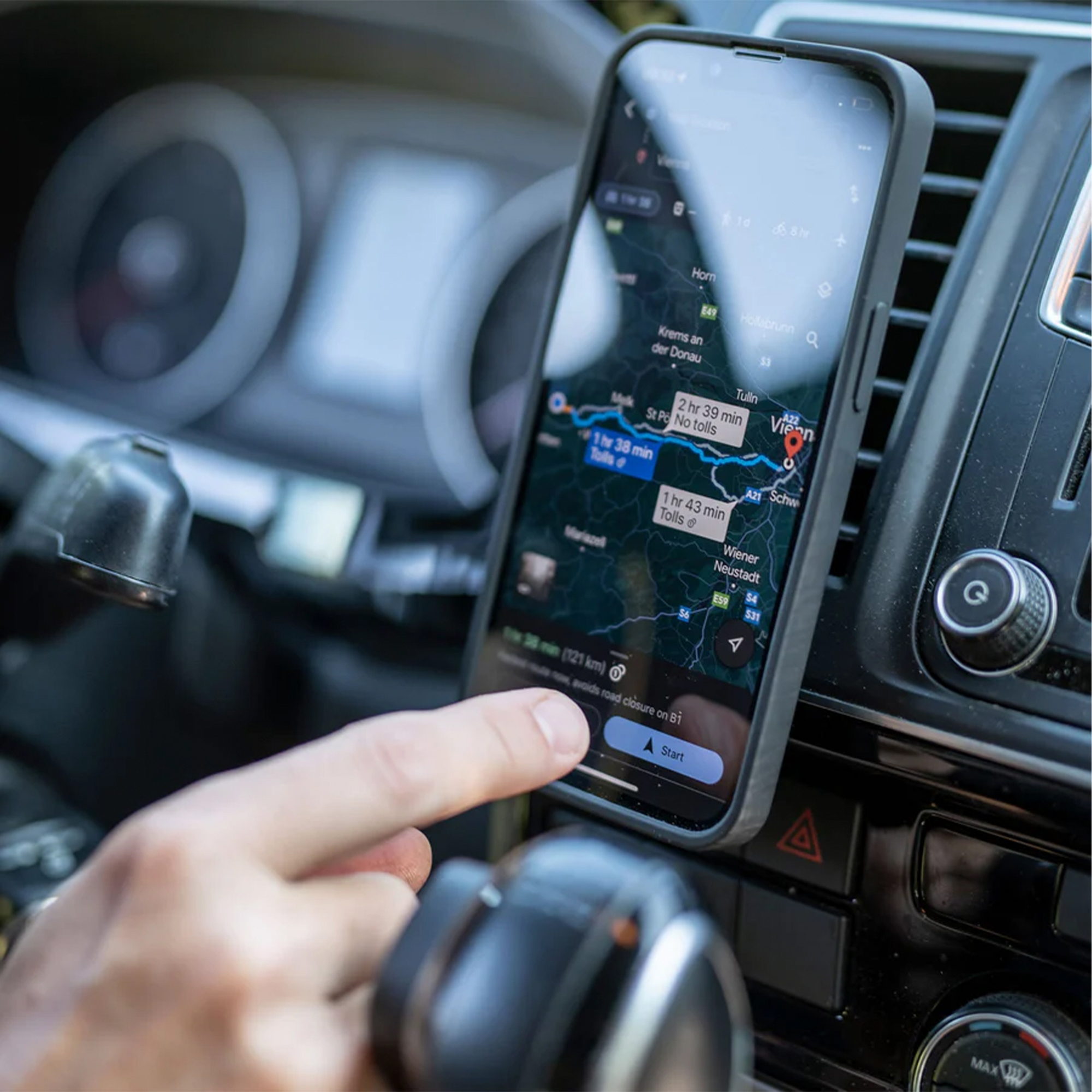 Eine Hand tippt auf ein Smartphone, das am Armaturenbrett eines Autos angebracht ist und eine Navigationskarte anzeigt.