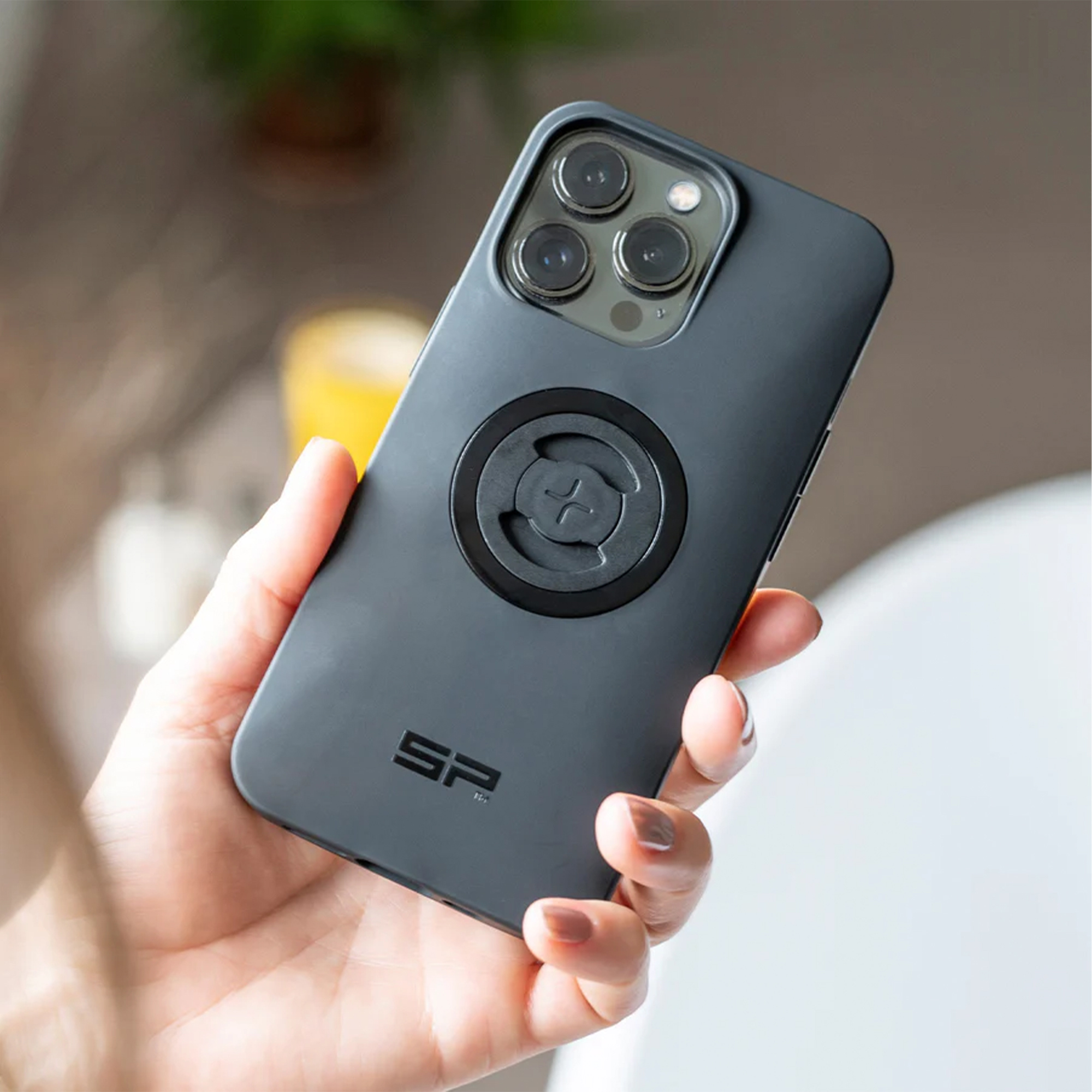 Eine Hand hält ein schwarzes Smartphone mit einer runden Halterung und dem SP Logo auf der Rückseite.