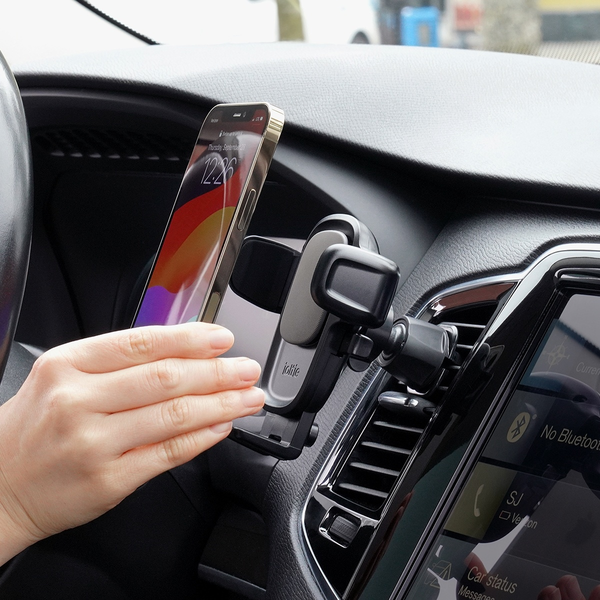 Eine Hand legt ein Smartphone in eine schwarze Halterung am Autolüftungsgitter.