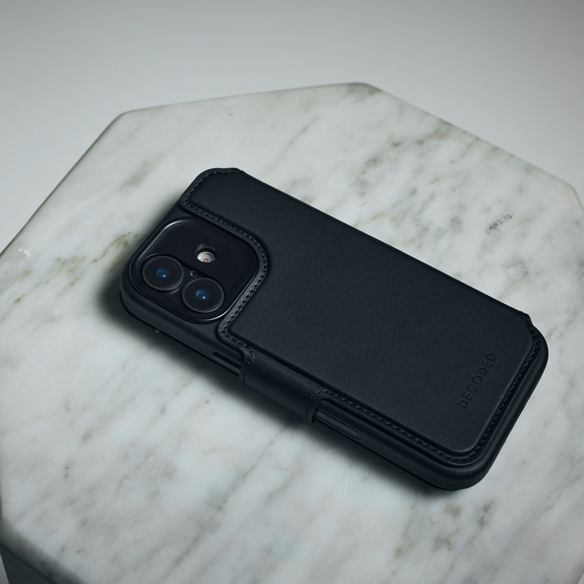 Ein schwarzes Smartphone mit Lederhülle und zwei Kameralinsen liegt auf einer weißen Marmorplatte.