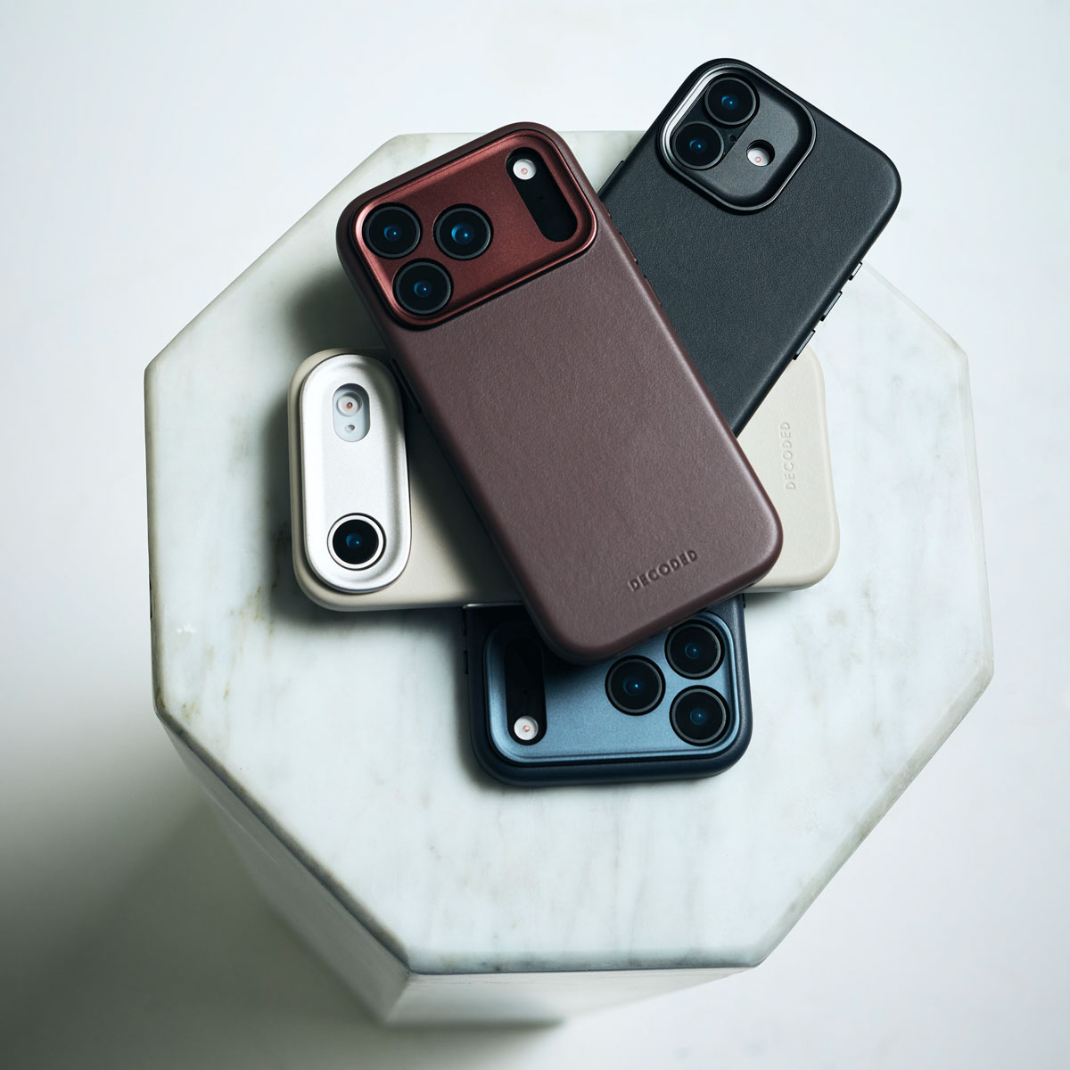Vier Smartphones in bunten Lederhüllen auf einem weißen Marmor-Sechskantständer.