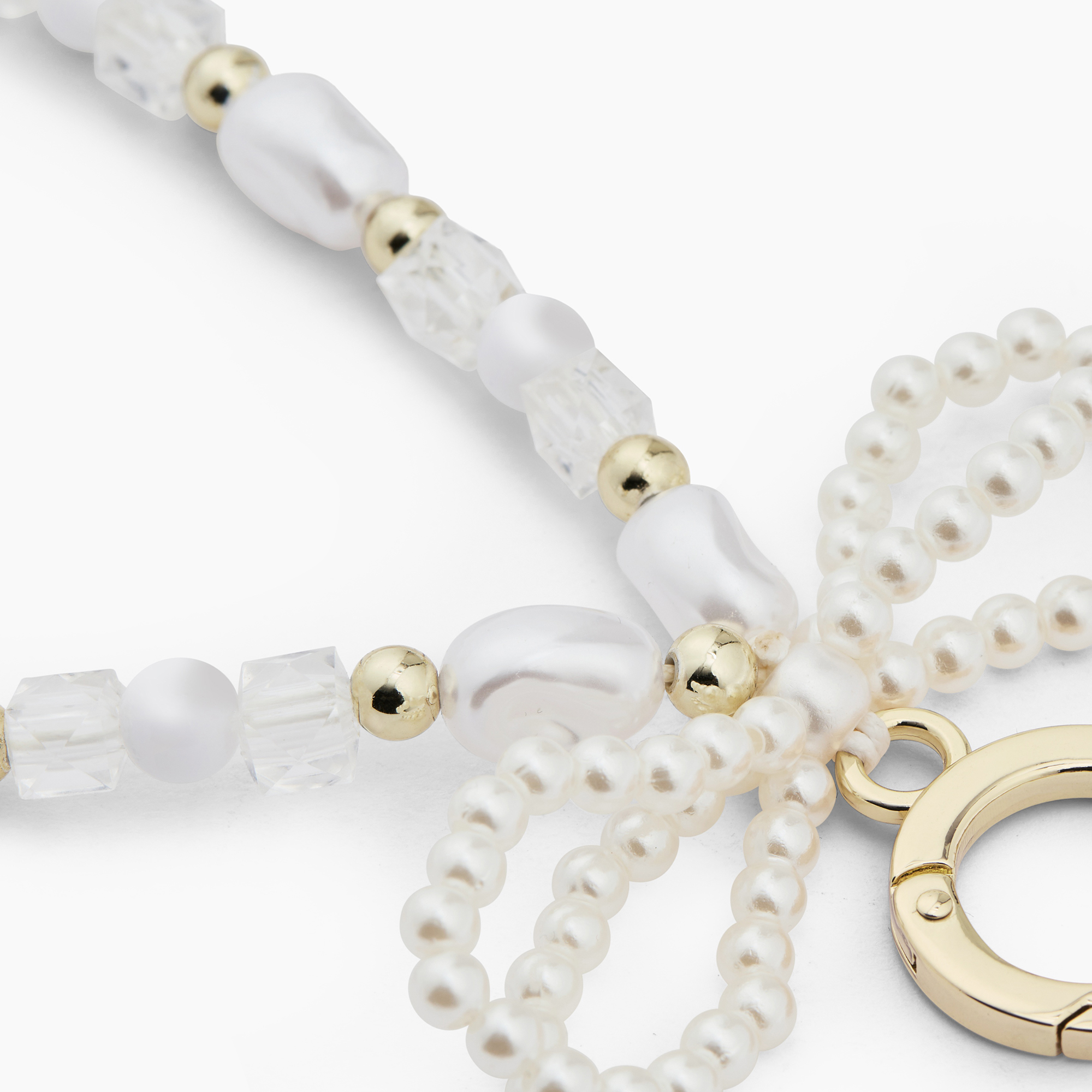 Nahaufnahme einer Halskette aus weißen Perlen, facettierten Kristallen, goldenen Kügelchen und einem goldenen Karabiner.