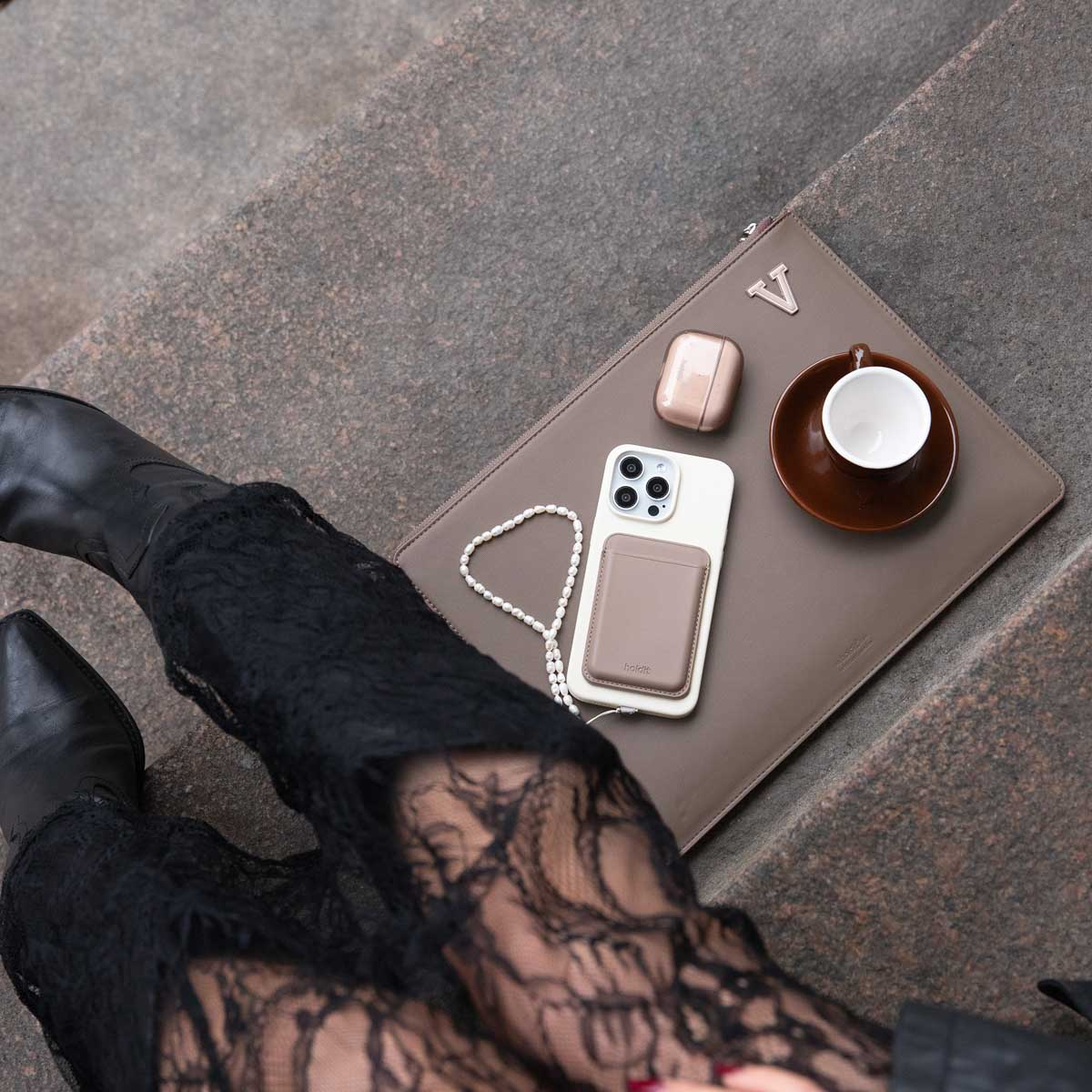 Person in Spitzenhosen und Stiefeln sitzt auf Steintreppen mit einer Tasche, Kaffeetasse, Telefon und Zubehör.