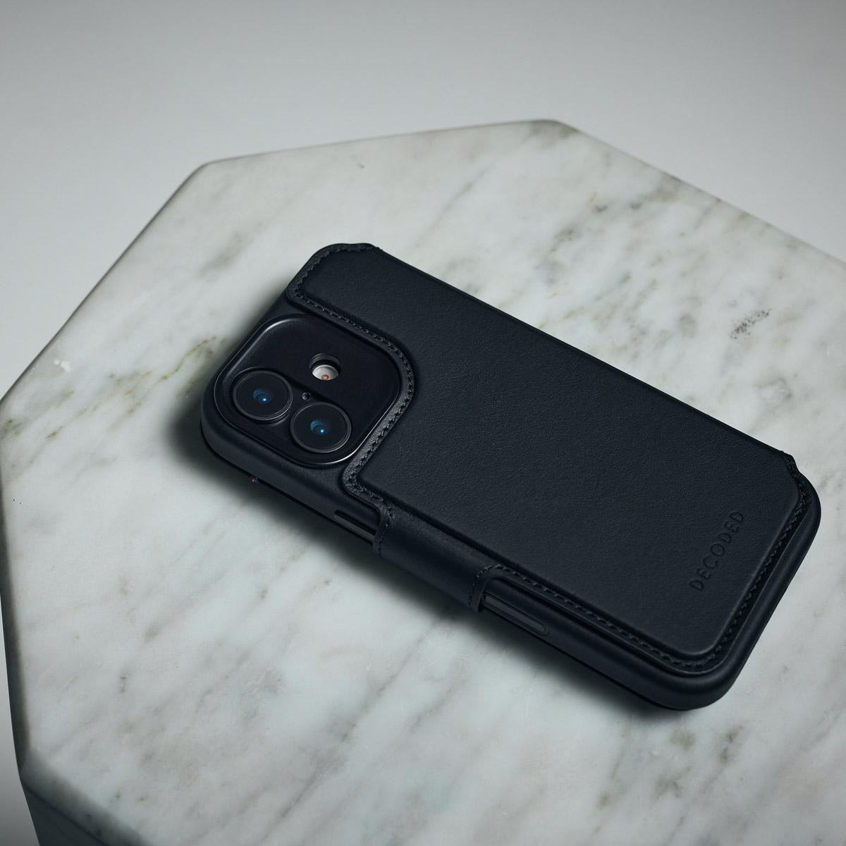 Eine schwarze Leder-Smartphone-Hülle mit Dual-Kamera-Ausschnitt liegt auf einer weißen Marmoroberfläche.