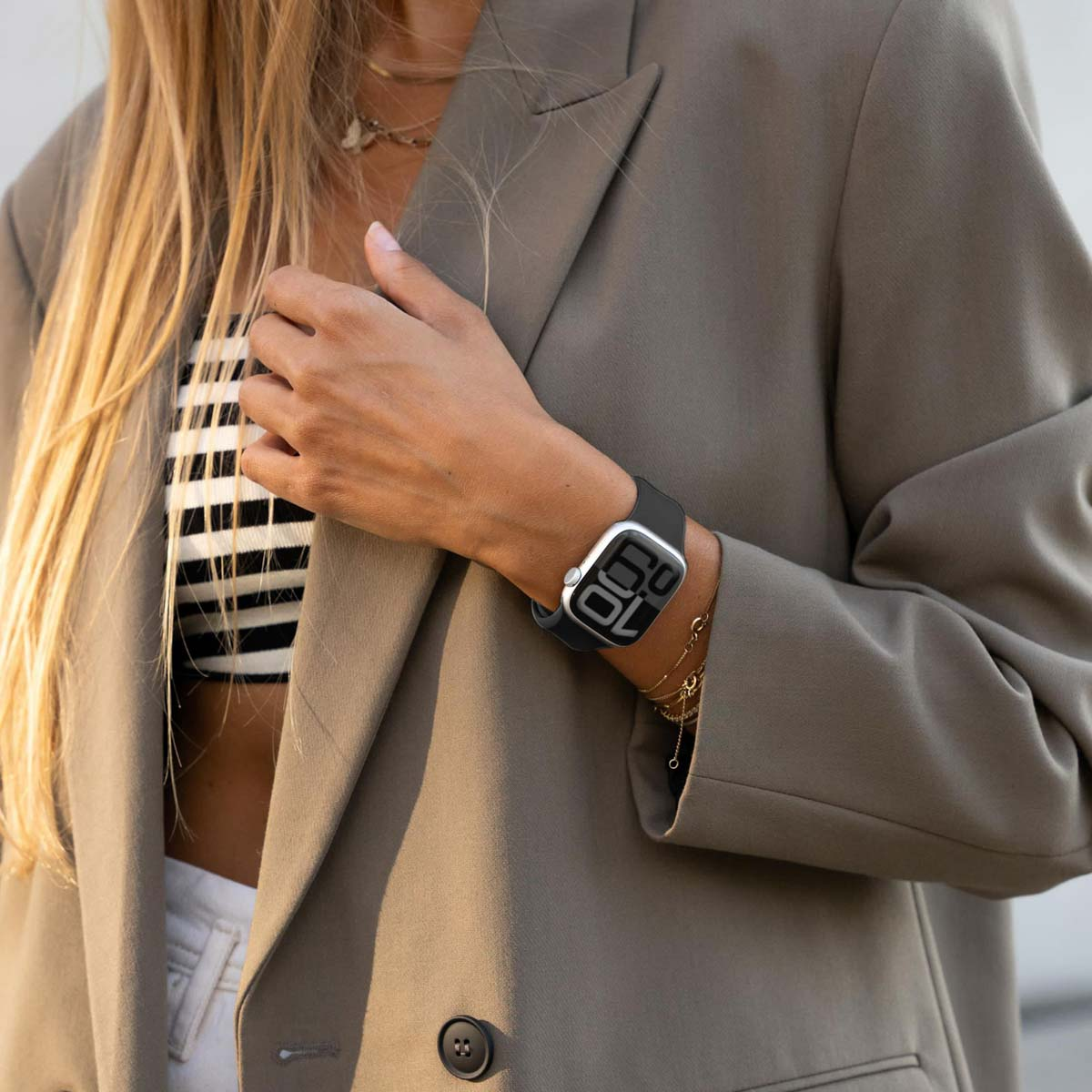 Blond kobieta w szarej marynarce nosi czarny smartwatch z cyframi.