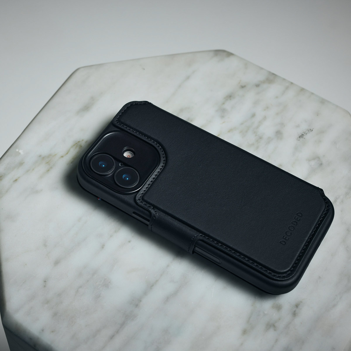 Ein schwarzes Smartphone in einer Lederhülle liegt auf einer weißen Marmorplatte.