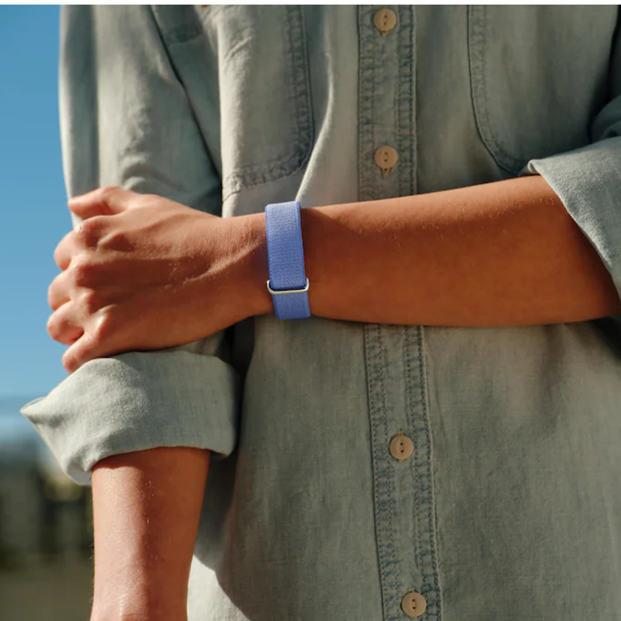 Eine Person im hellblauen Jeanshemd trägt ein blaues Stoffarmband am Handgelenk.
