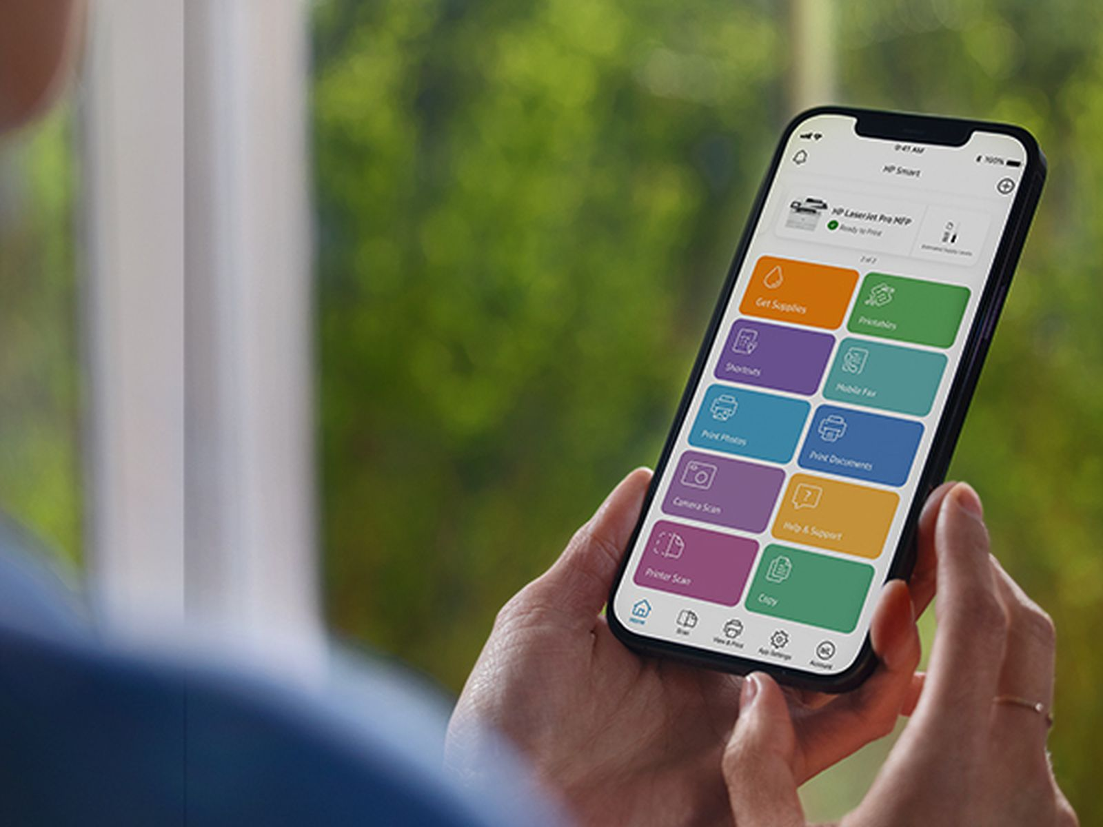 Eine Person hält ein Smartphone mit einer bunten App-Oberfläche vor verschwommenem grünem Hintergrund.
