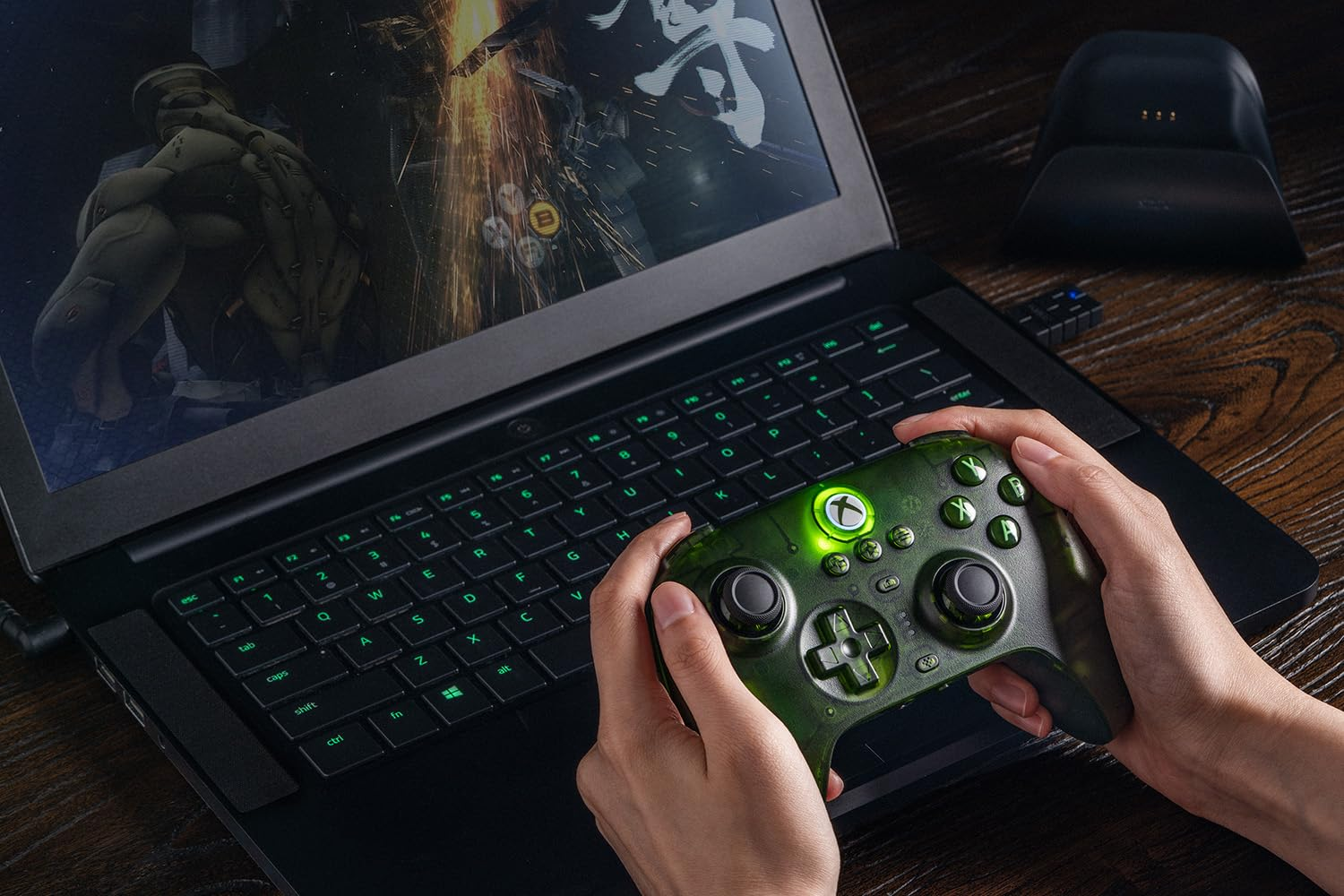 Ręce trzymające przezroczysty zielony kontroler Xbox, grające na laptopie.