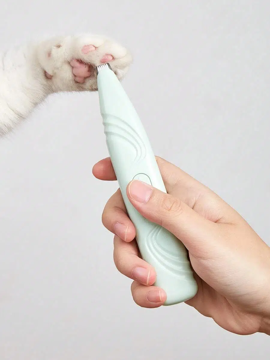 Bir el, beyaz bir kedinin patisindeki tüyleri kesmek için nane yeşili bir tıraş makinesi tutuyor.