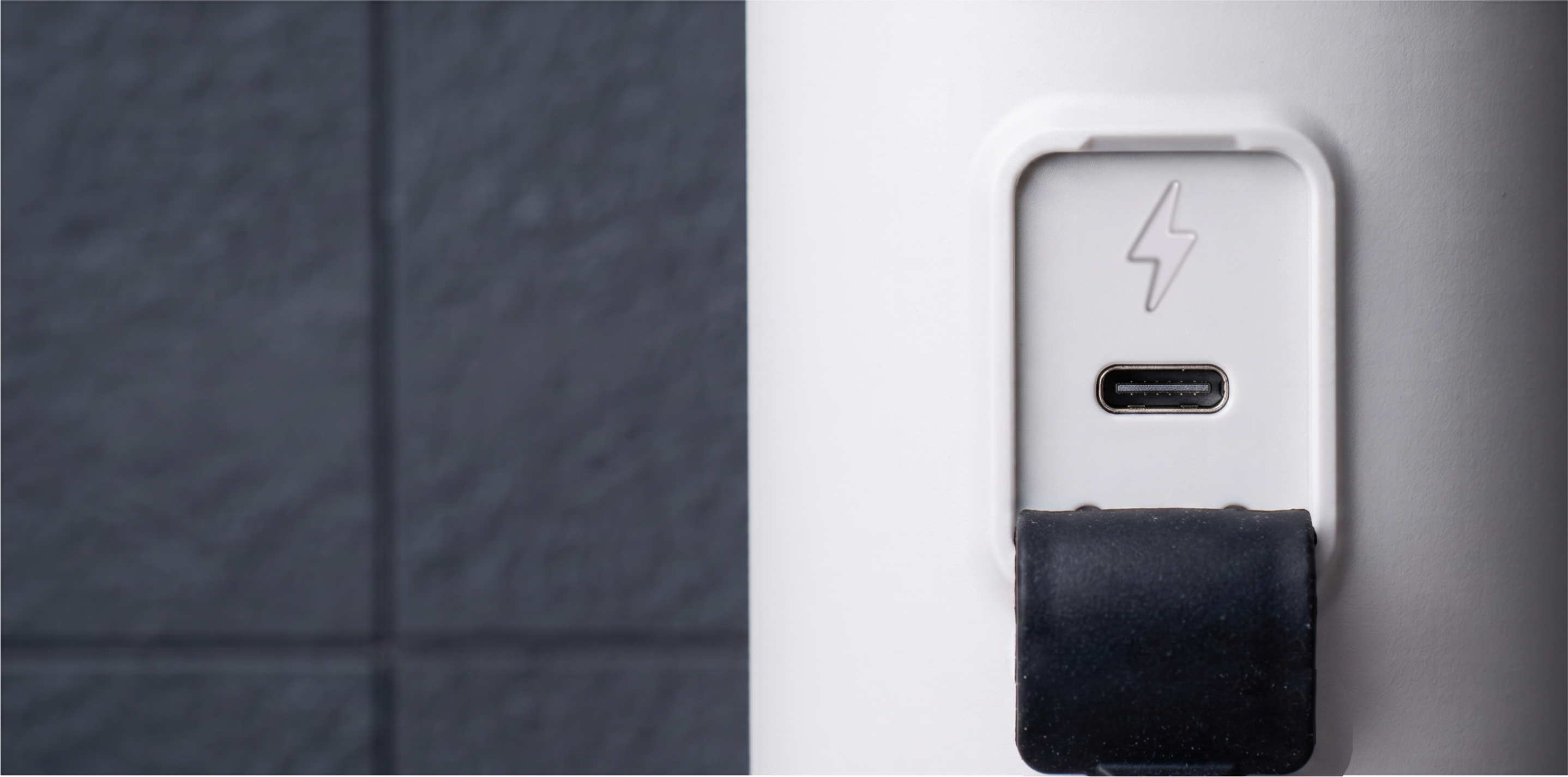 Port USB-C na białym urządzeniu z symbolem błyskawicy powyżej i otwartą czarną gumową klapką.
