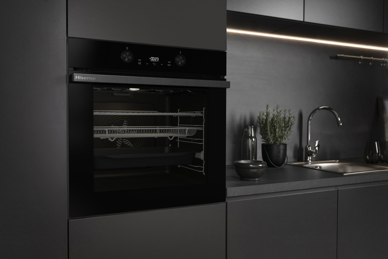 Moderno horno empotrado Hisense negro en una cocina oscura y elegante con fregadero y plantas.