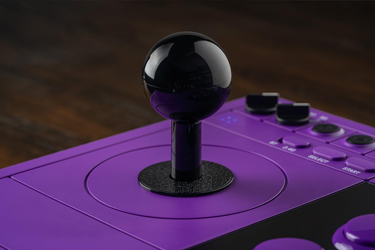 Błyszczący czarny joystick z gałką na fioletowym kontrolerze arcade na ciemnym drewnie.