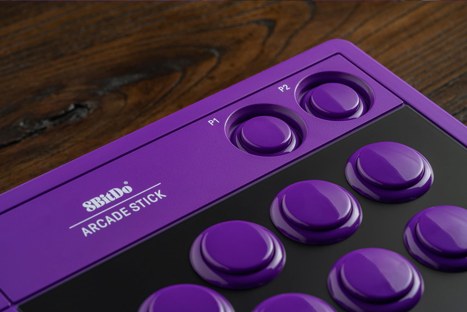 Zbliżenie fioletowego joysticka arcade 8BitDo z okrągłymi przyciskami na drewnianym stole.