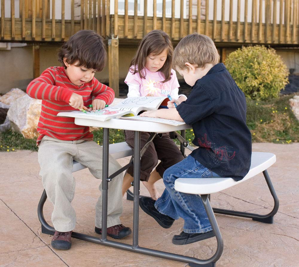Drei kleine Kinder sitzen an einem Tisch im Freien und malen in Malbücher.