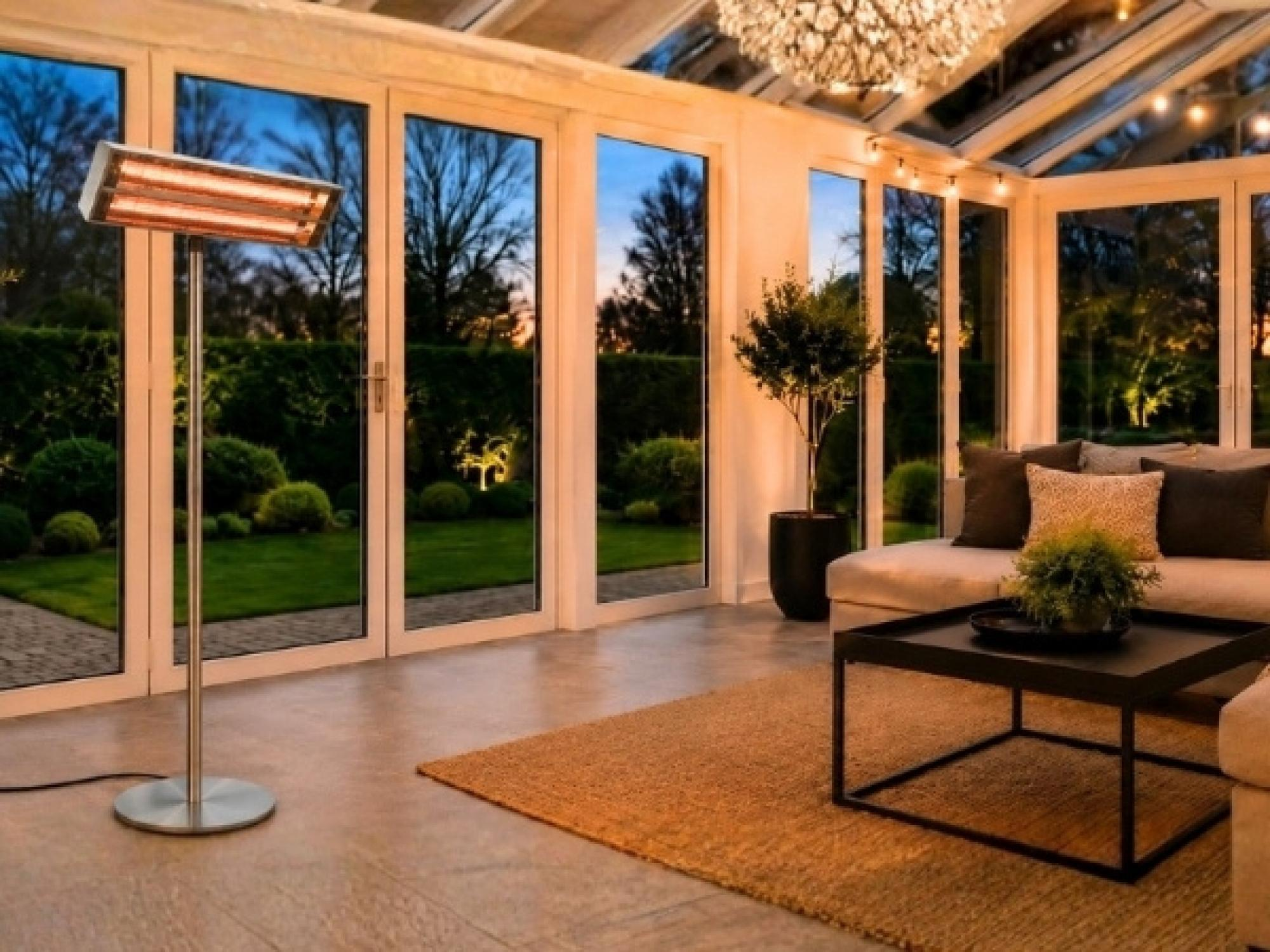 Ein moderner Terrassenstrahler steht in einem hellen Wintergarten mit großen Fenstern, einem Sofa und einem Couchtisch.