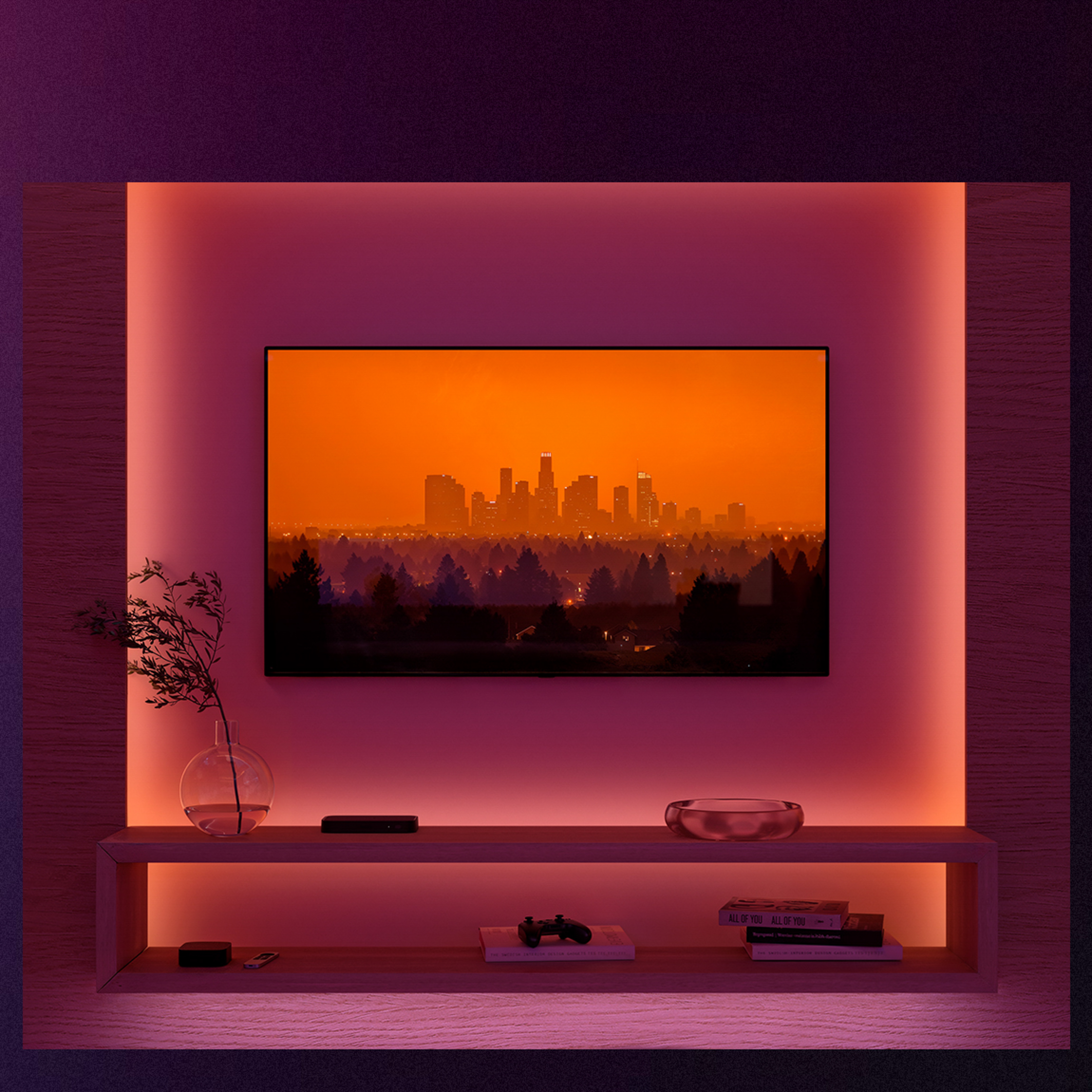 Una TV su una parete illuminata di rosa con skyline e ripiani sottostanti con decorazioni.
