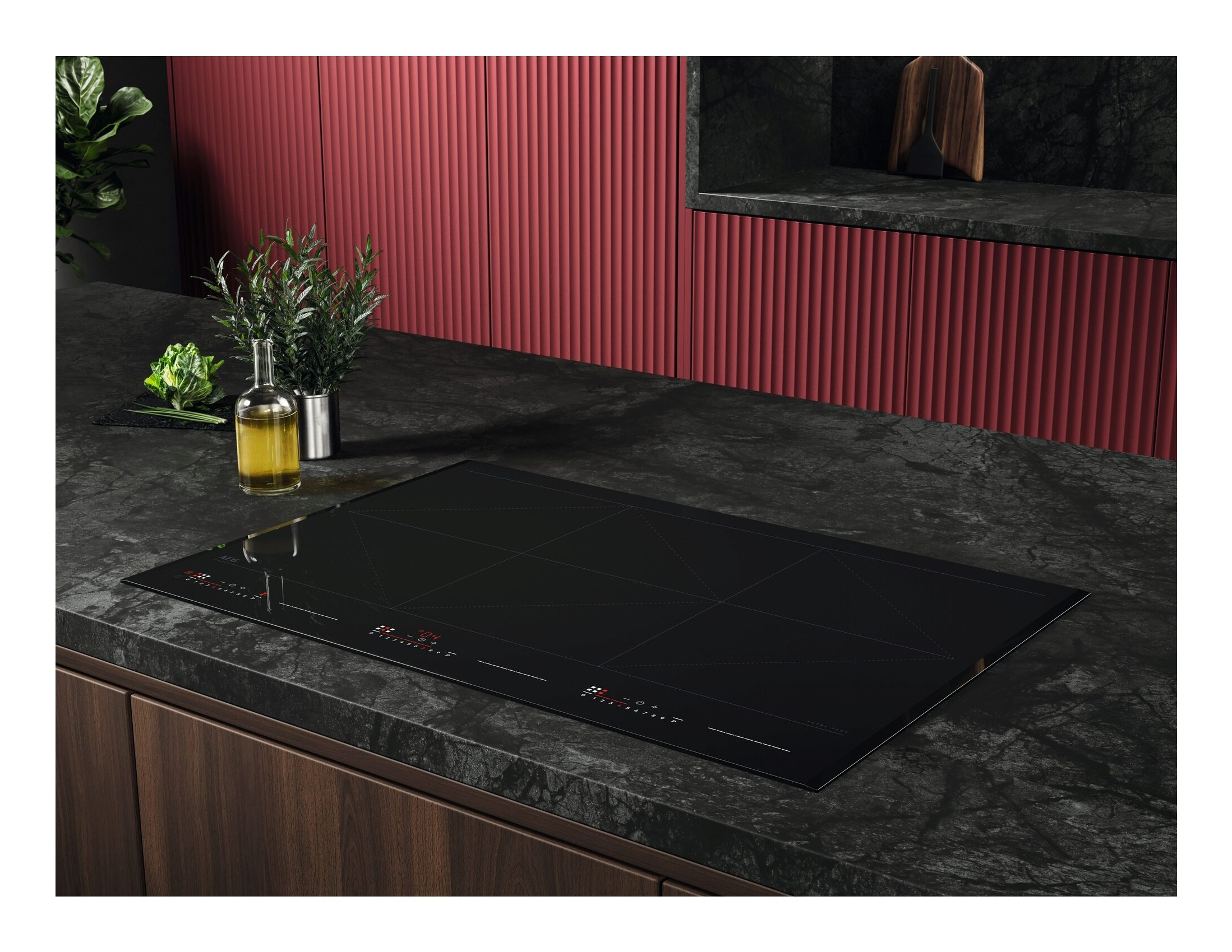 Un piano cottura a induzione nero su un piano di lavoro in marmo scuro in una cucina moderna con mobili rossi.