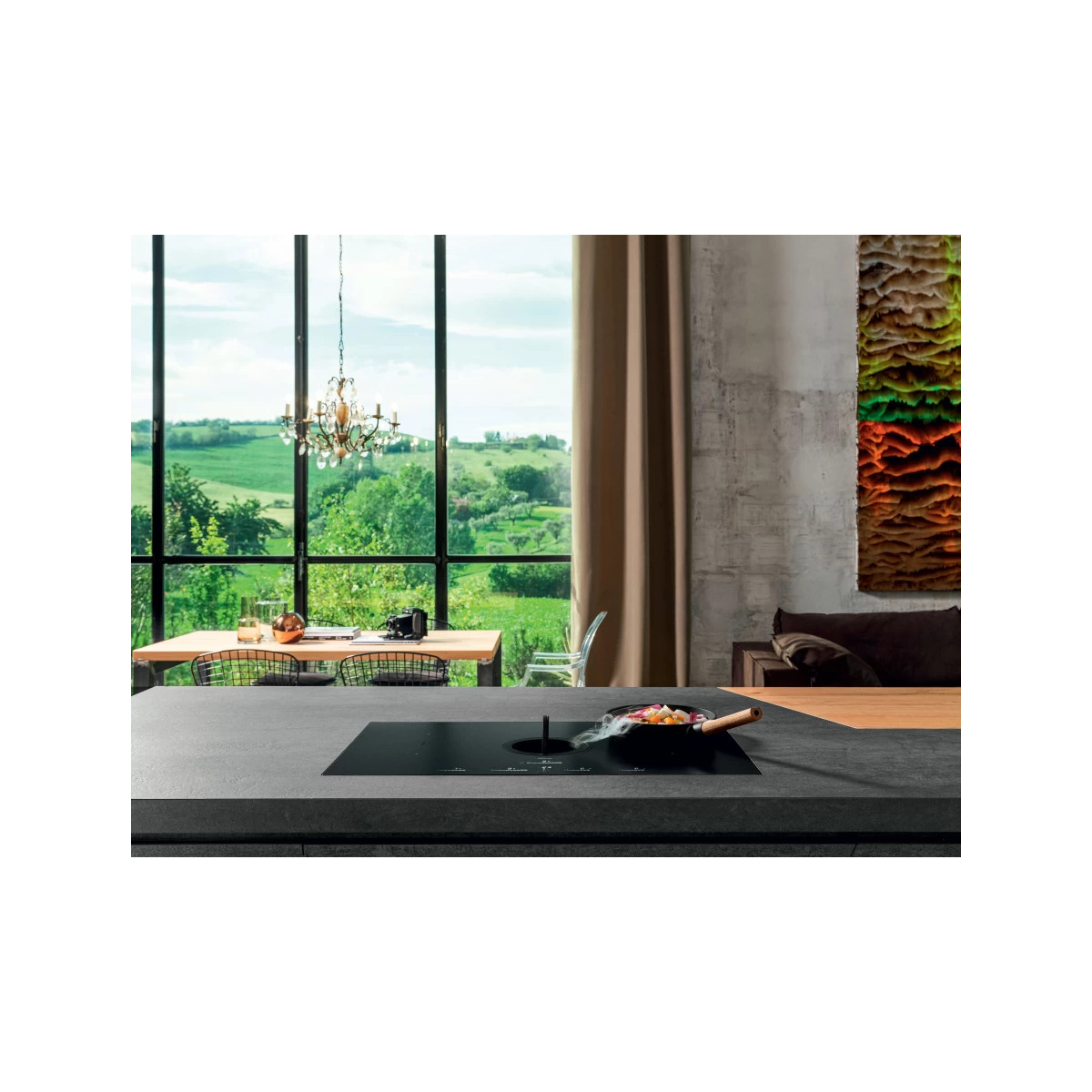 Un piano cottura nero con estrattore integrato su un bancone grigio scuro in una cucina moderna con vista su un paesaggio verde.