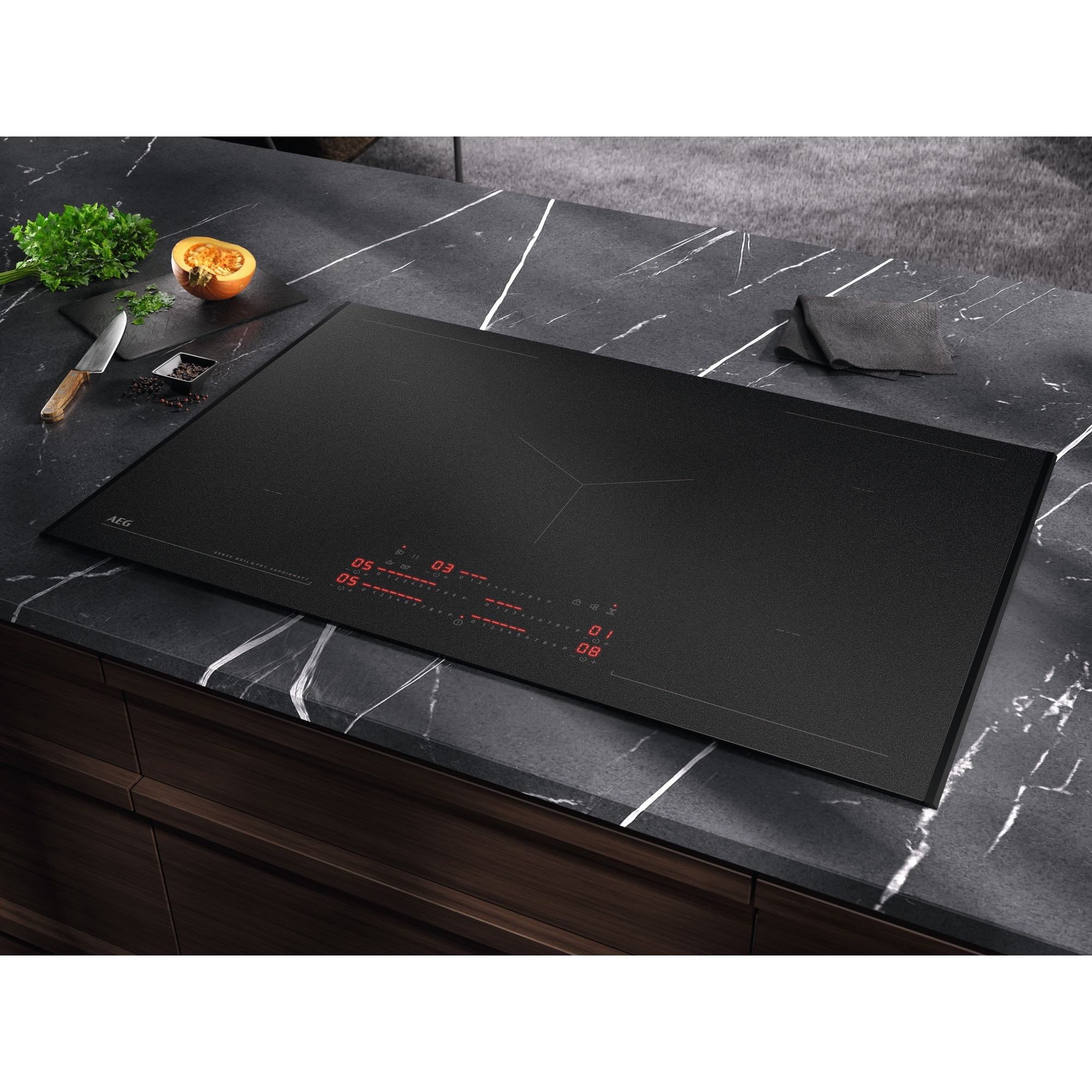Un piano cottura a induzione nero è incassato in un piano di lavoro in marmo scuro con ingredienti.