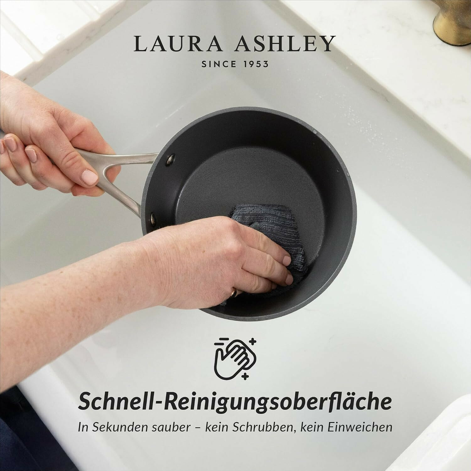 Hände reinigen eine graue Pfanne mit einem Tuch im weißen Spülbecken.
