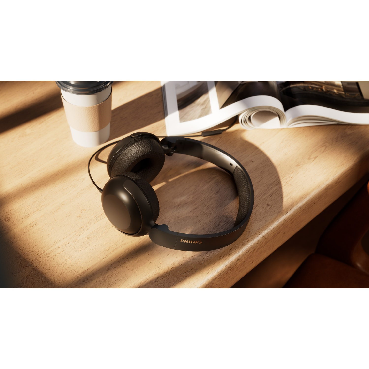 Cuffie Philips nere, un bicchiere e una rivista aperta su un tavolo di legno al sole.