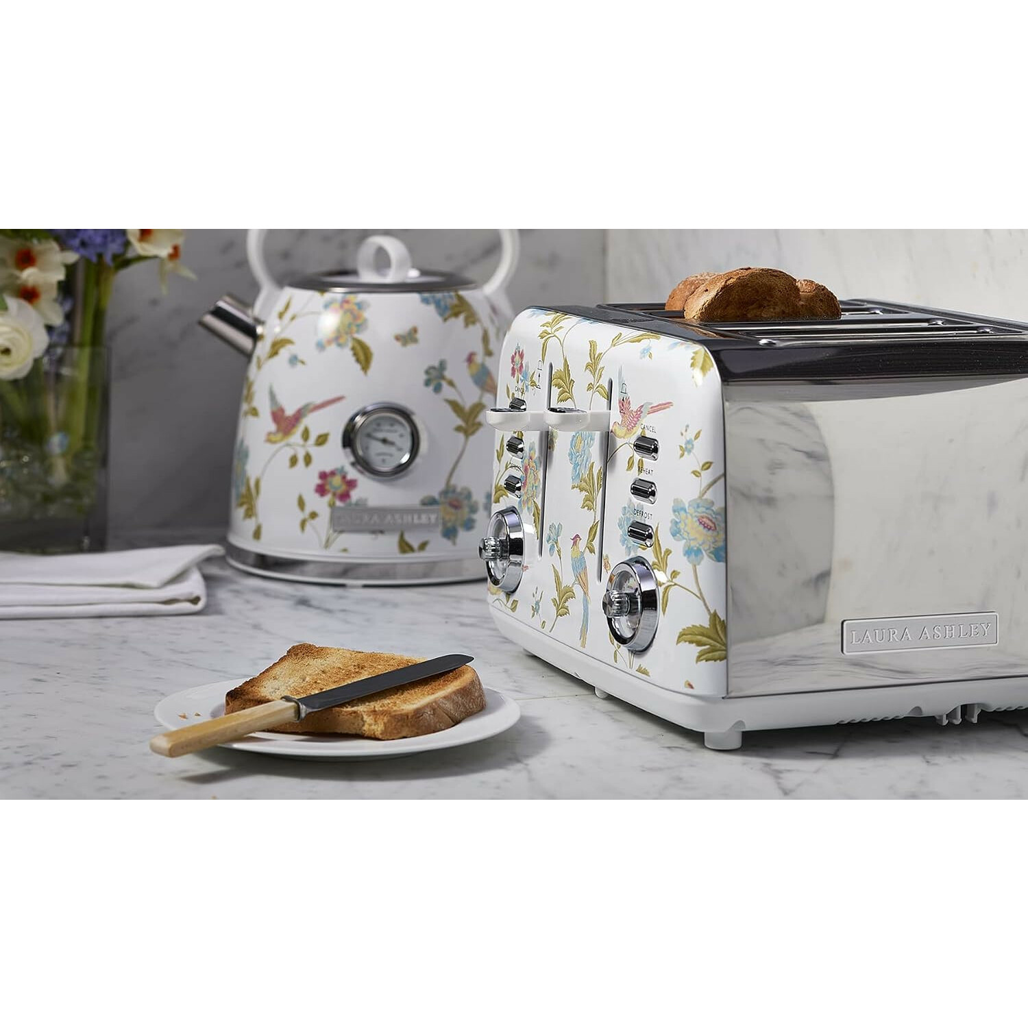 Ein weißer Toaster und Wasserkocher mit Blumenmuster, Toast auf einem Teller und in den Schlitzen auf einer Marmorarbeitsplatte.