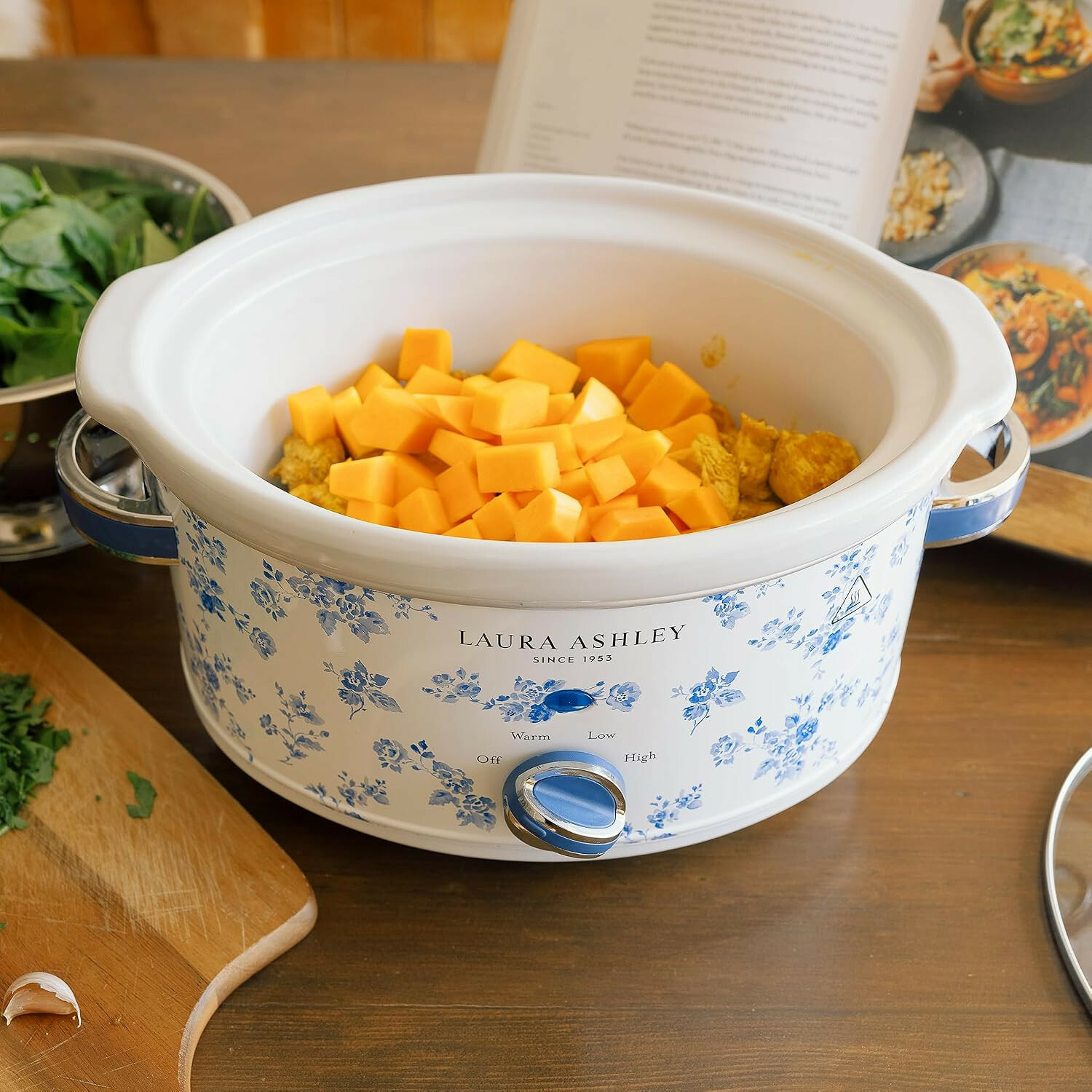 Ein weißer Laura Ashley Slow Cooker mit blauem Blumenmuster enthält Kürbiswürfel und Fleisch auf einem Holztisch.