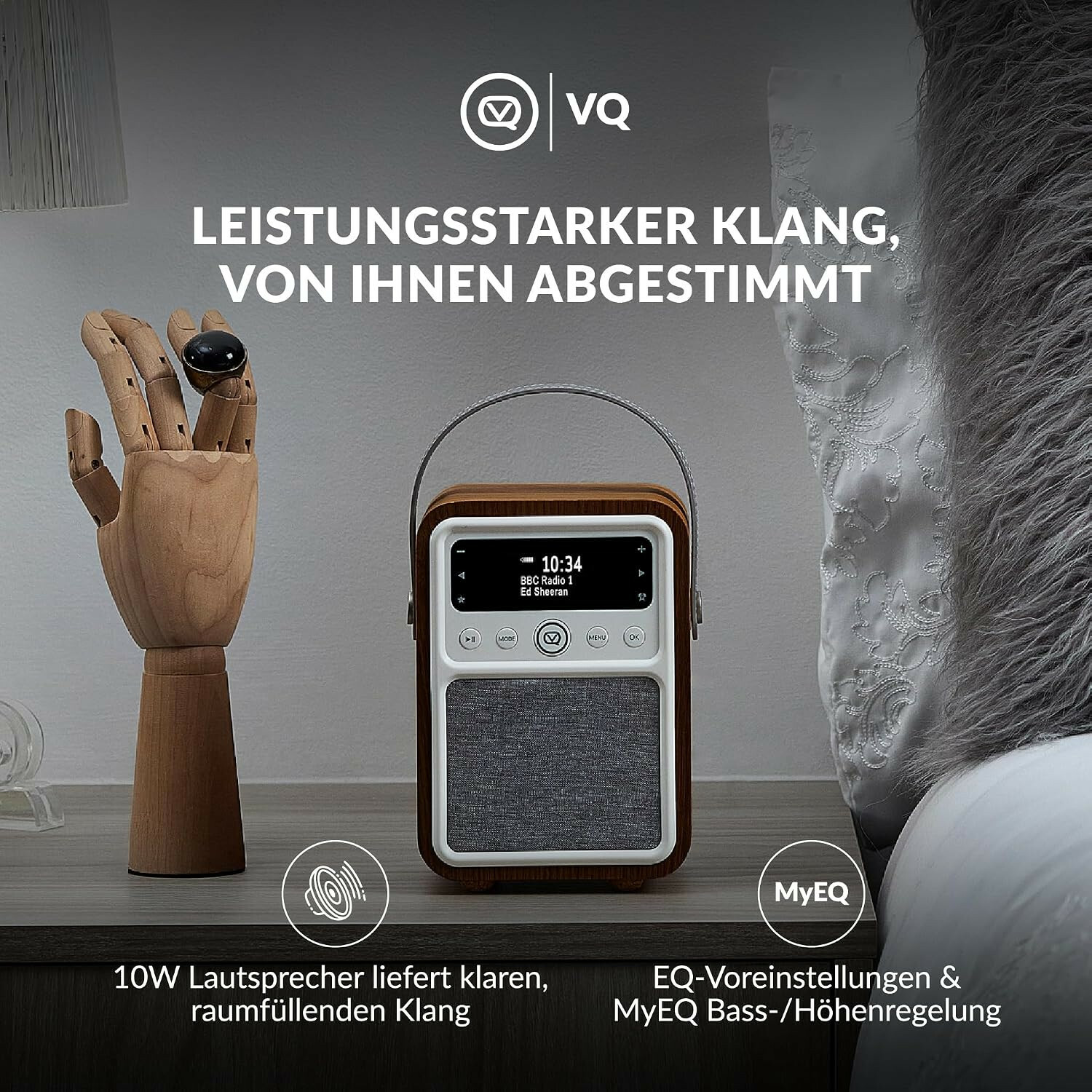 Ein VQ-Radio auf einem Nachttisch neben einer Holzhand mit Ring und einem Kissen.